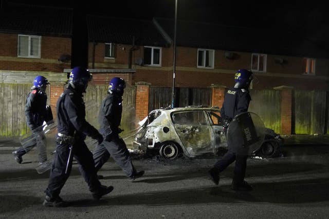 Police Officers walk past a burnt out police vehicle as they are deployed on the streets of Hartlepool (Owen Humphreys/PA)