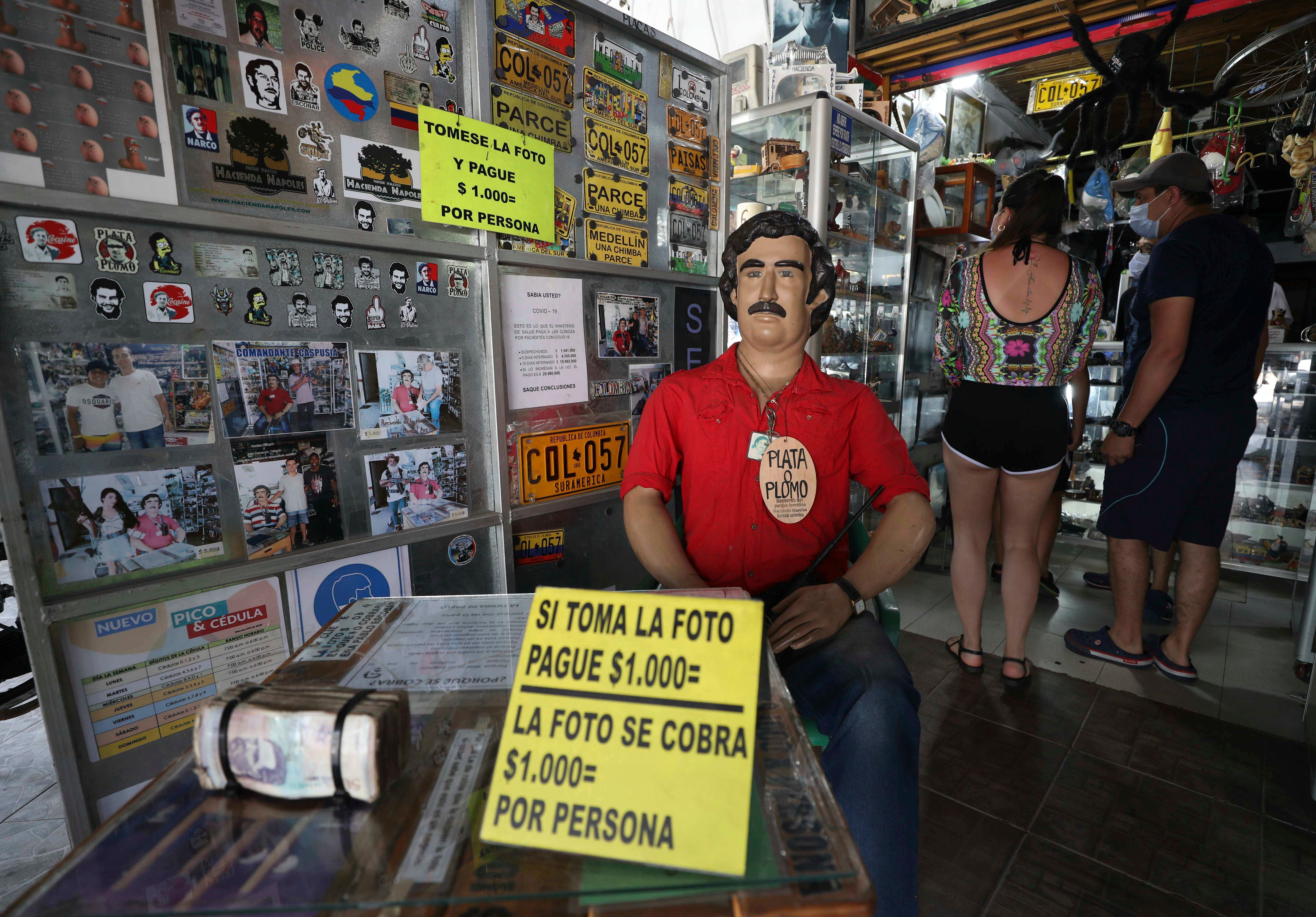 Tourists buy souvenirs of the late drug lord Pablo Escobar, featured as a statue with a sign that says one will be charged for taking photos inside a store in Doradal, Colombia, Feb. 5, 2021