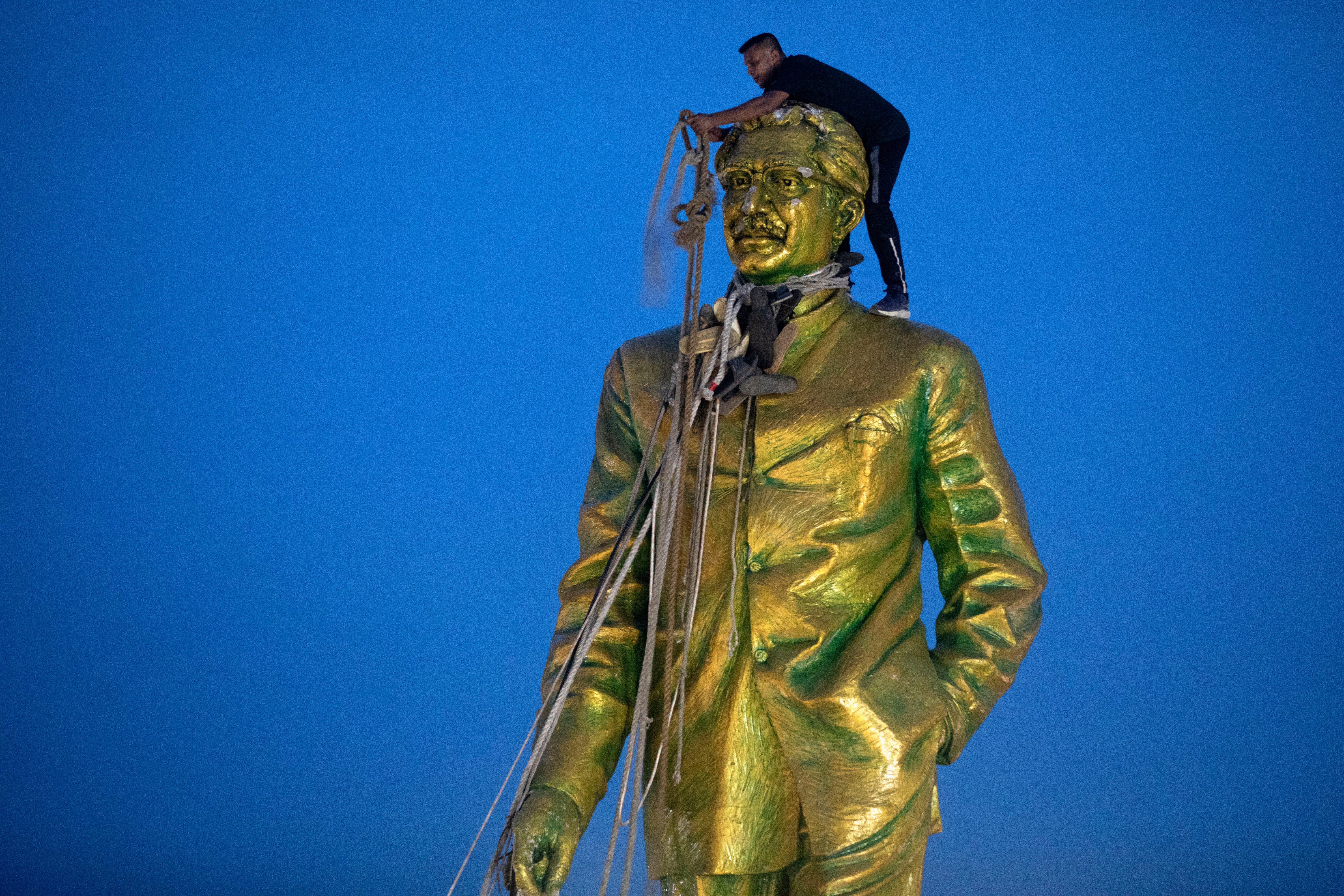 A man climbs to tie a rope around the head of a large statue of Sheikh Mujibur Rahman, father of Bangladesh leader Sheikh Hasina