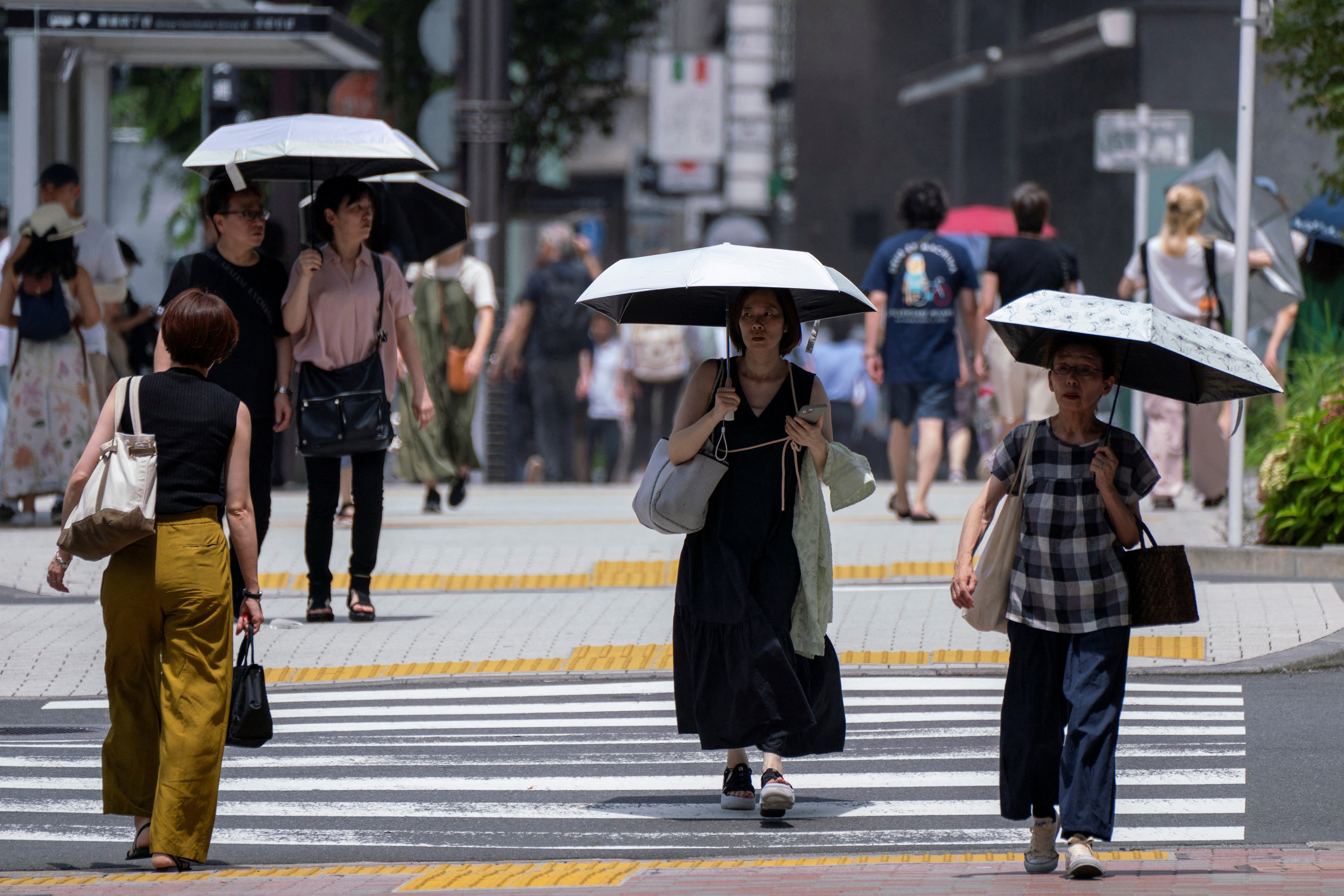 Pedestrian with parasols walk along a sidewalk during hot weather in central Tokyo