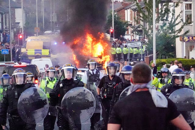 <p>Riot police hold back protesters near a burning police vehicle after disorder broke out on July 30, 2024 in Southport, England</p>