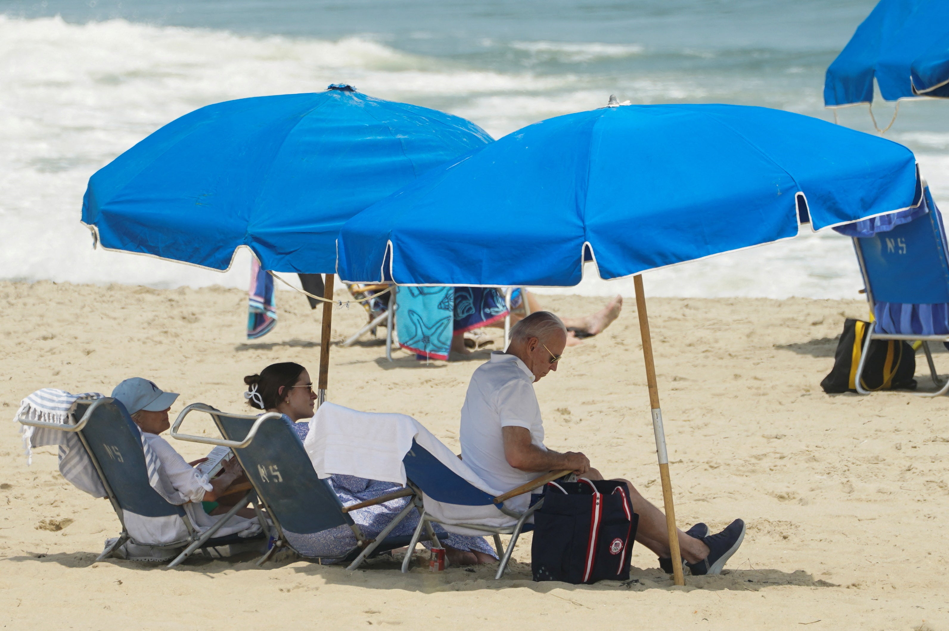 President Joe Biden, granddaughter Naomi and first lady Jill Biden sit under an umbrella at Rehoboth Beach in Delaware