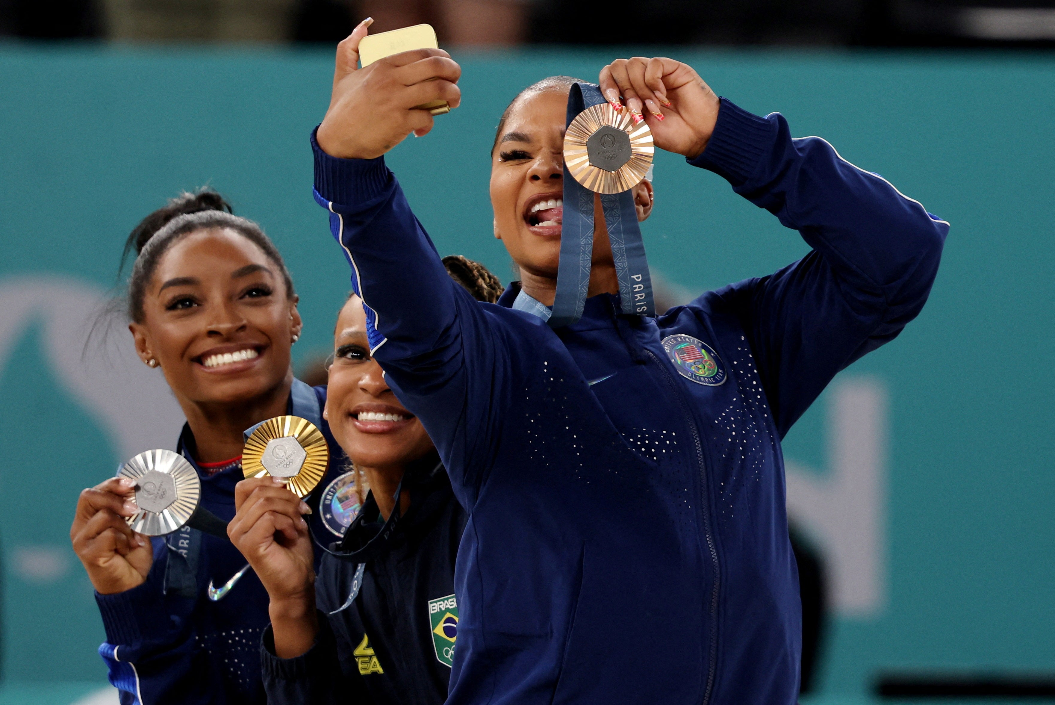 Bronze medalist Jordan Chiles takes a photo next to gold medalist Rebeca Andrade and silver medalist Simone Biles. Chiles had to return her bronze medal following the decision of an independent governing body