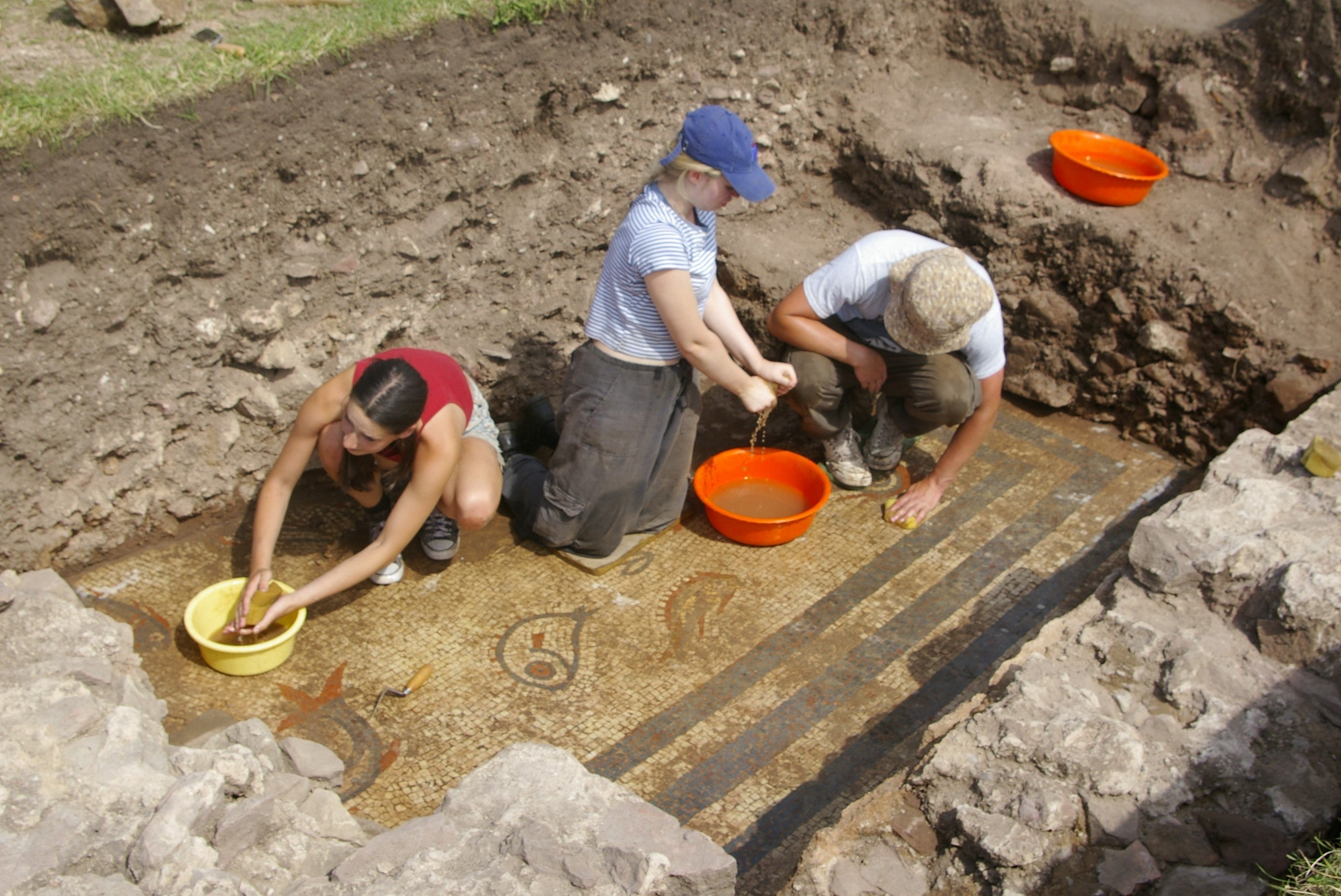 Archaeologists cleaning a rare 2,000-year-old mosaic depicting dolphins