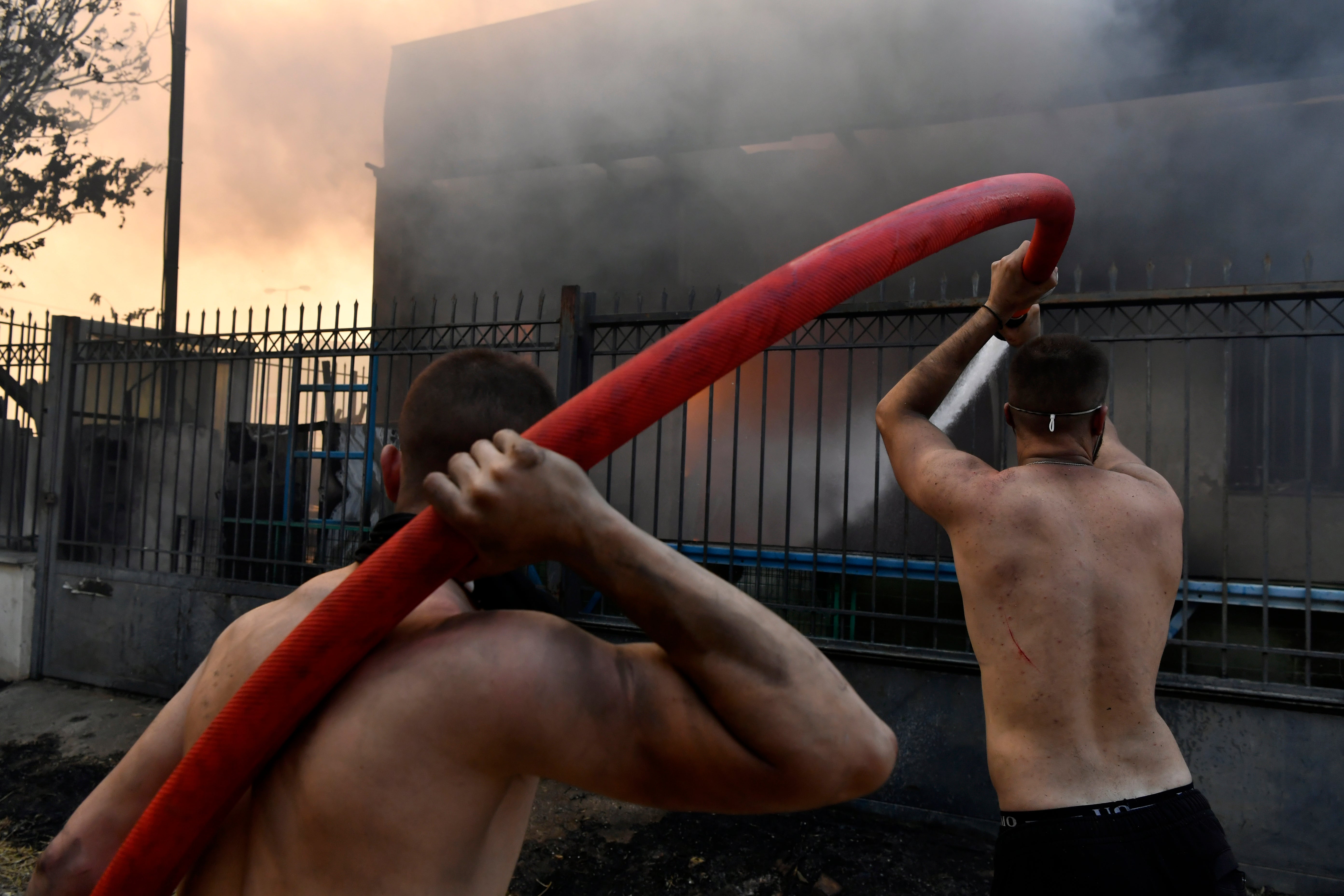 Two men try to extinguish the flames at a burning business during a fire in northern Athens, Monday