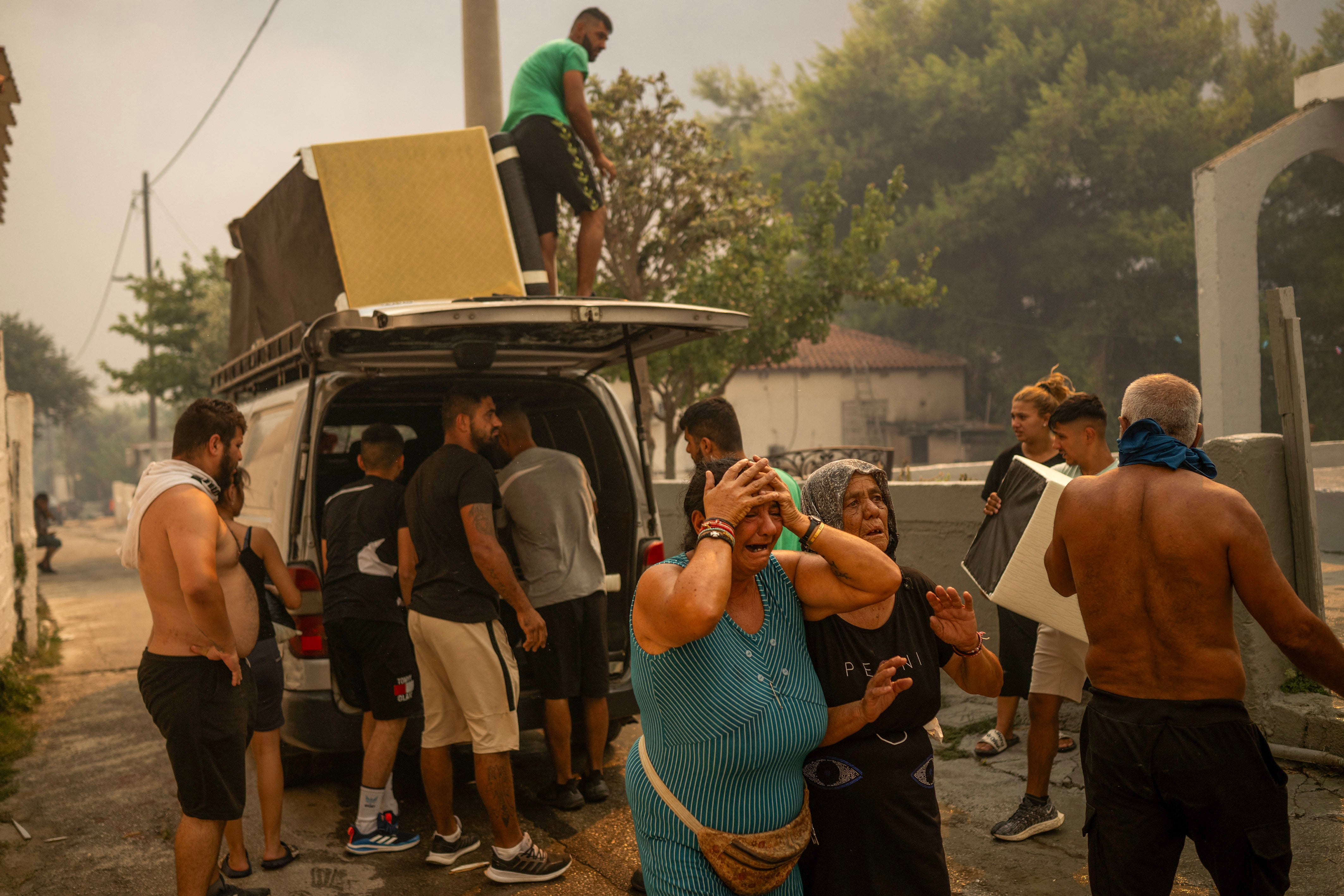 Local residents cry as they try to save some belongings during a wildfire near Penteli