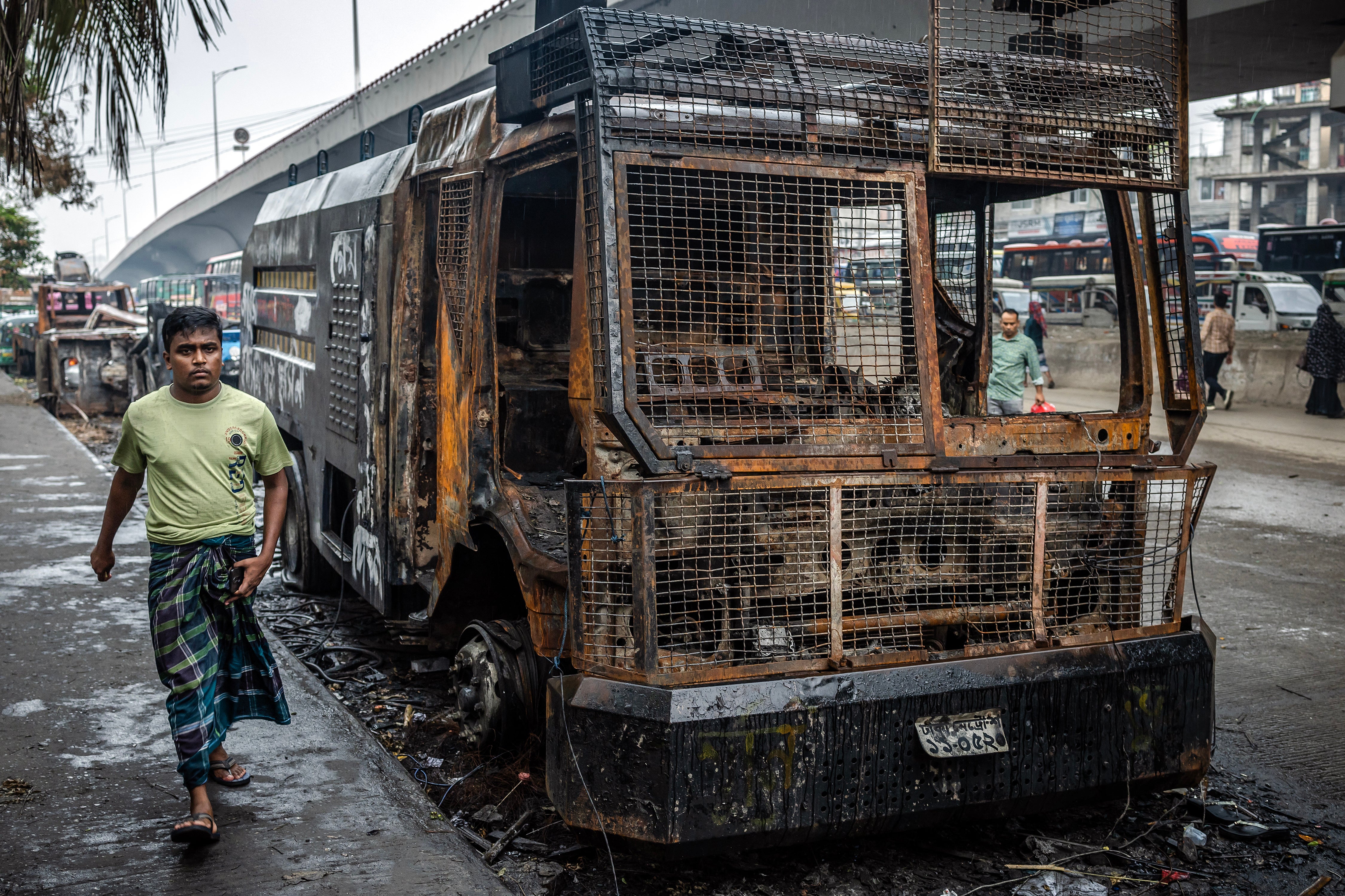 A man walks past a police water cannon truck that was burned during the protests against Sheikh Hasina’s government