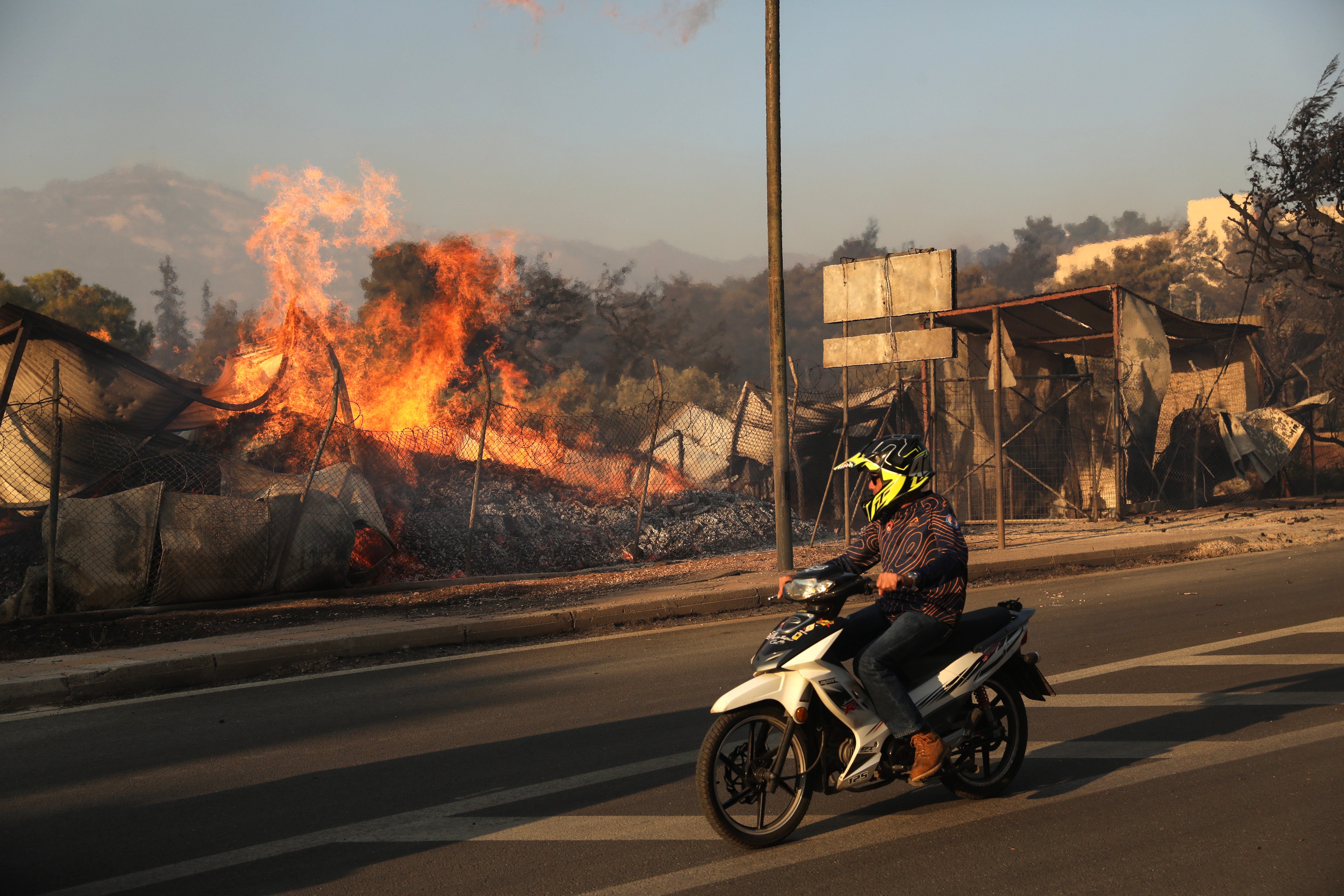 A person riding a scooter watches as a wildfire engulfs a firewood business, in Penteli, northeast of Athens, Greece