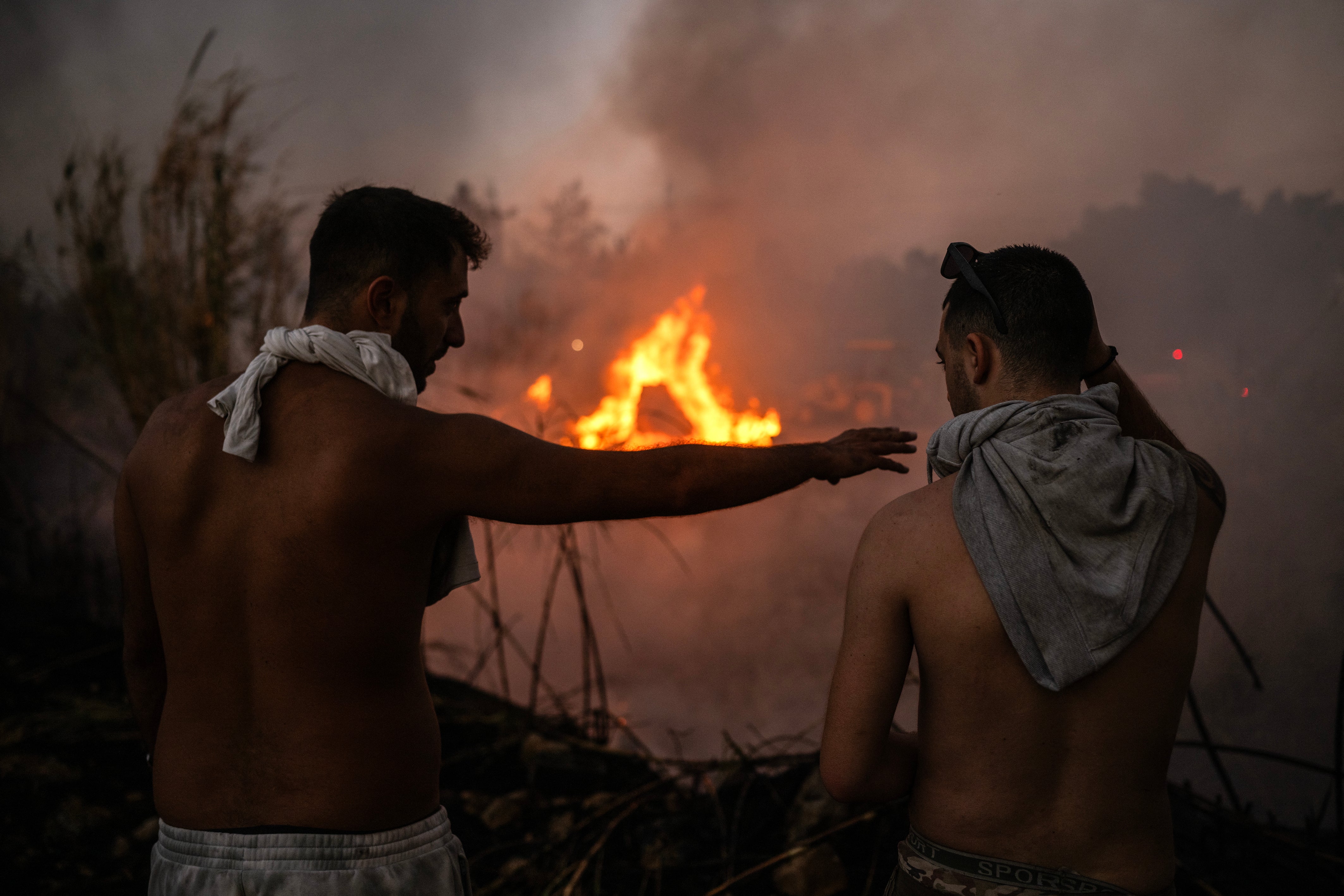 Volunteer stand in front of a small pocket of fire as wildfires burn near Penteli