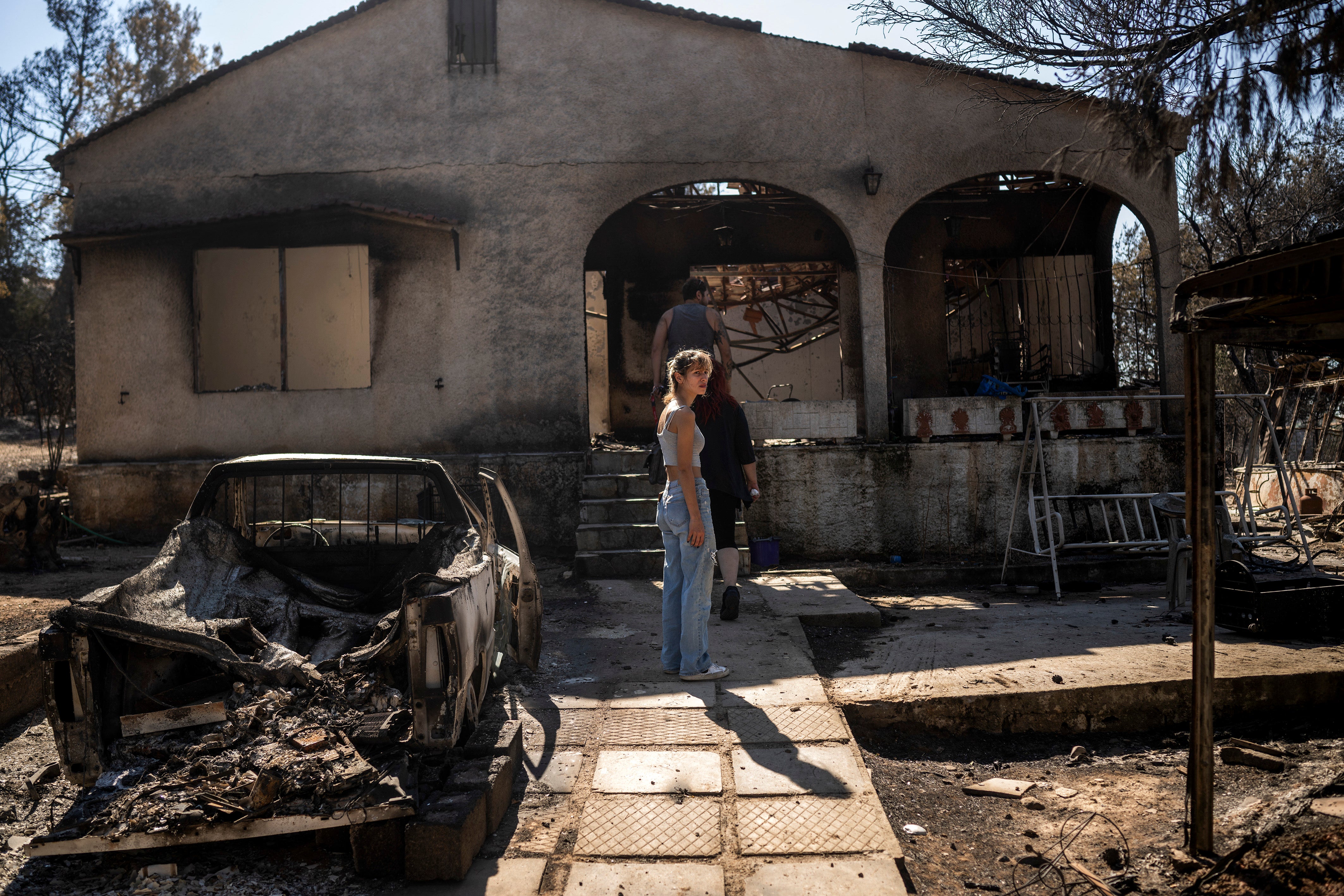 Owners look at the damage to their burnt home following a wildfire that hit the north-eastern suburbs of Athens, in Chalandri, suburb of Athens