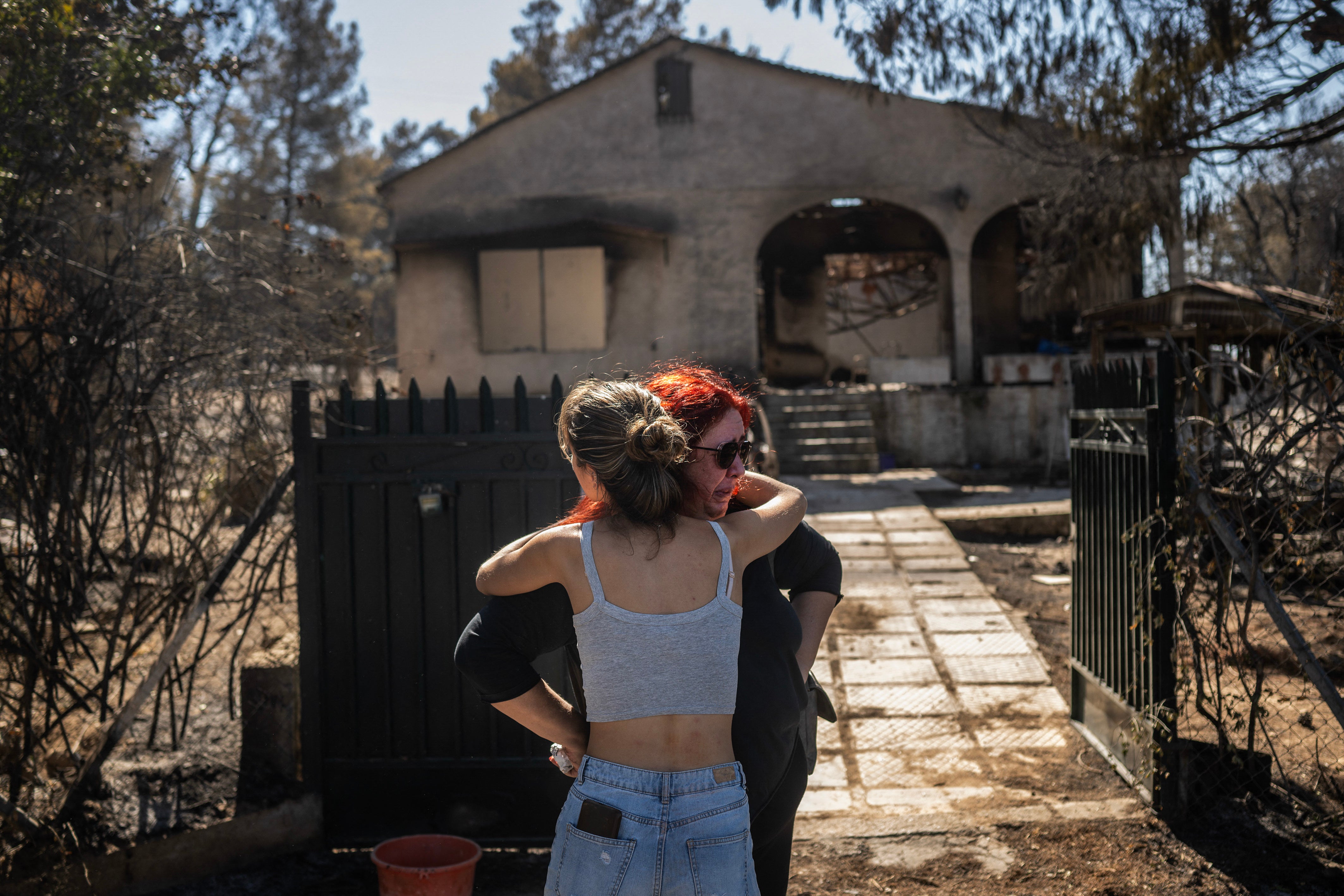 Relatives comfort each other after looking at the damage to their burnt home following a wildfire that hit the north-eastern suburbs of Athens, in Chalandri