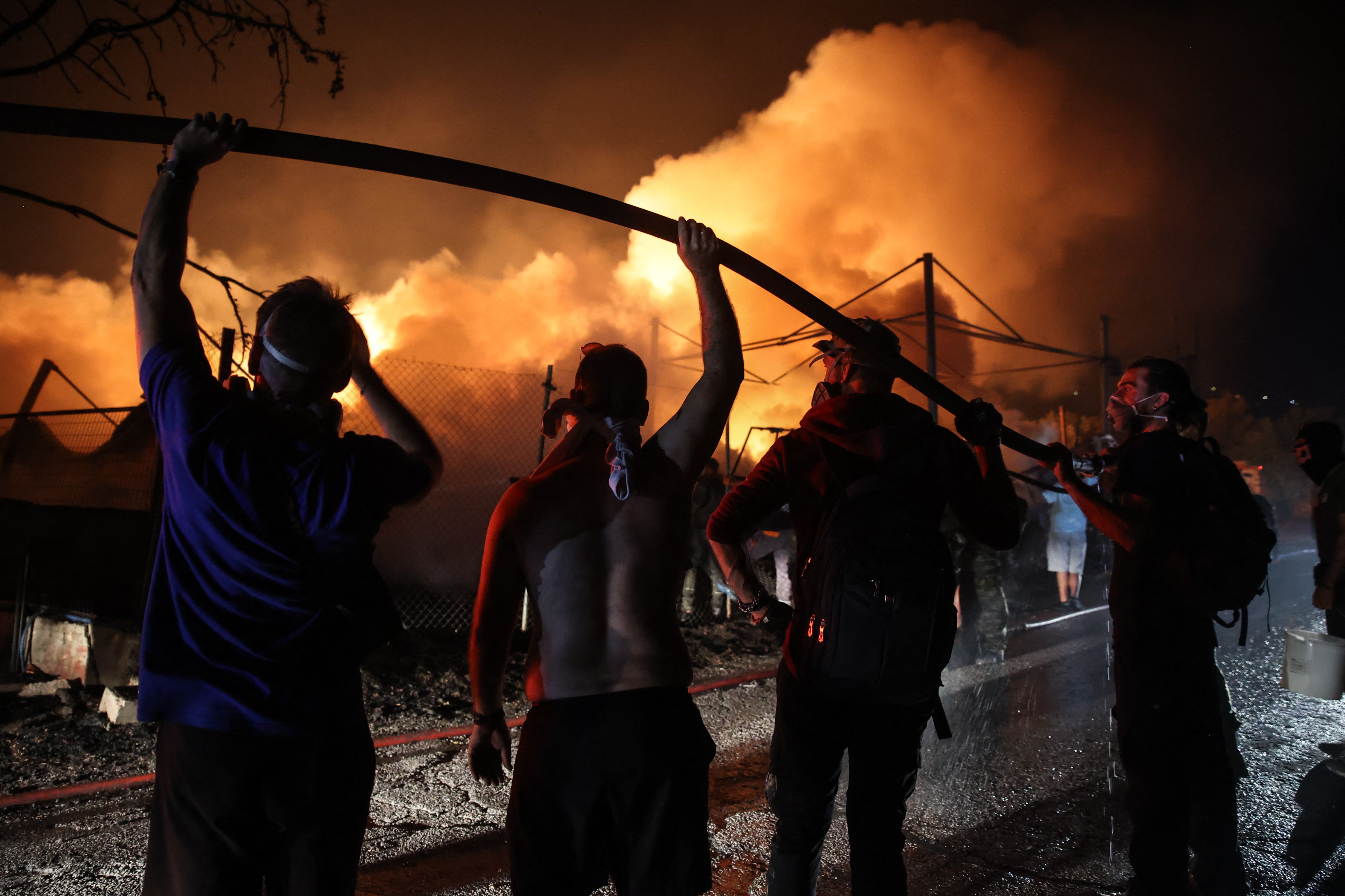 Volunteers hold a water hose in order to help firefighters extinguish a fire in a wood factory in Vrilissia, on the outskirts of Athens