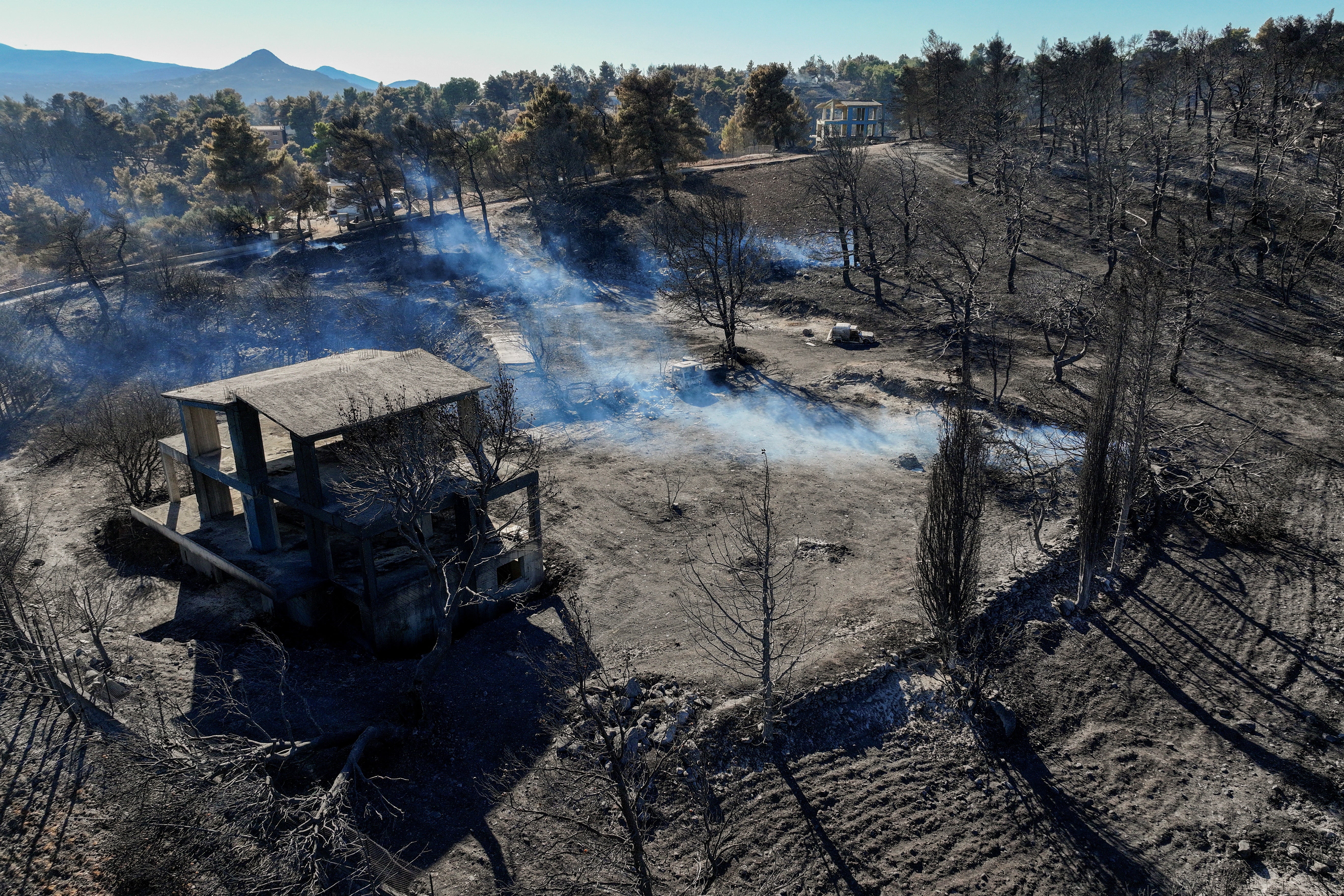 A drone view shows smoke rising in a charred forest area following a wildfire, in the village of Varnavas, Greece