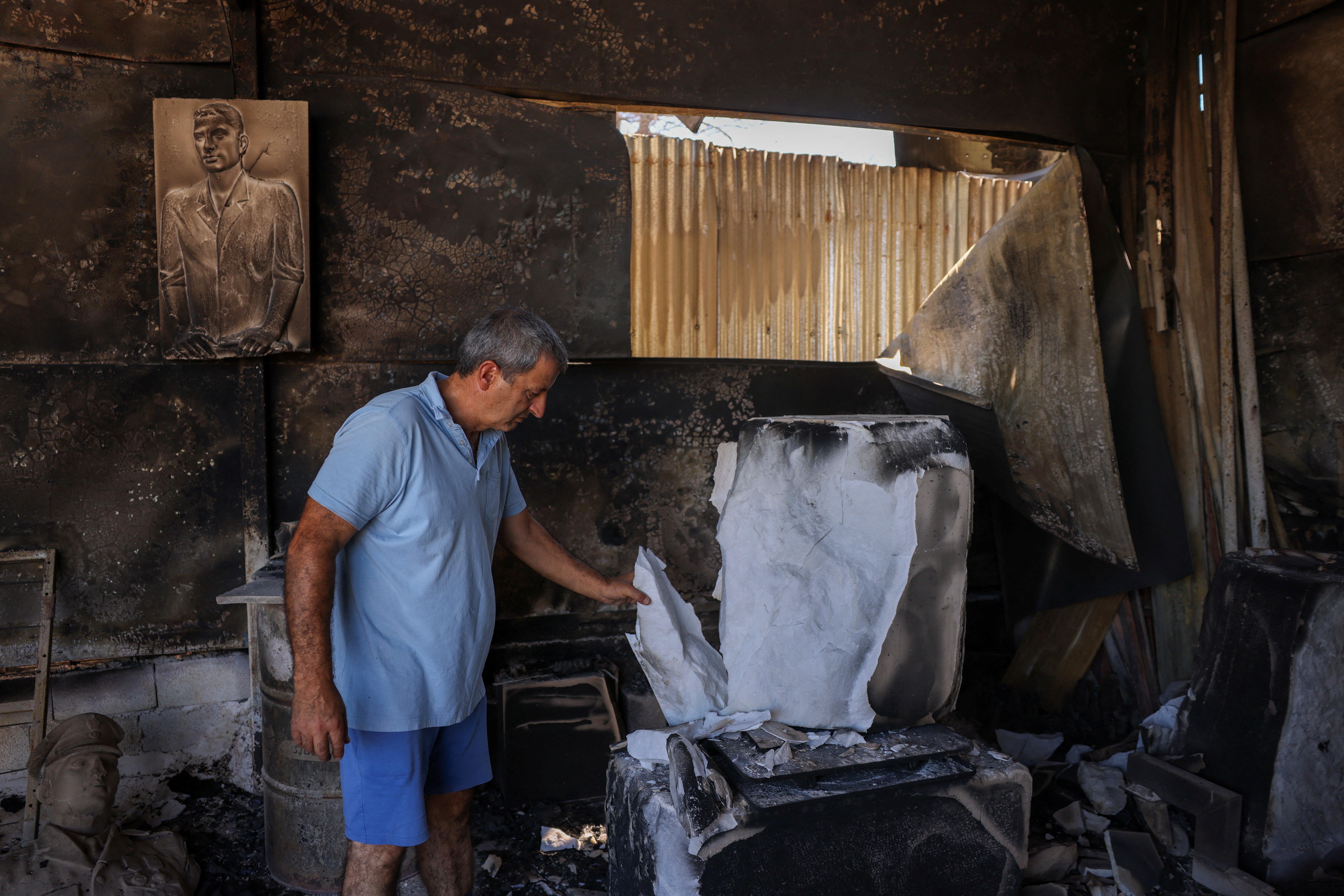 Vangelis Elias, 55, examines damaged sculptures in his destroyed workshop after a wildfire in Brilisia, near Athens.