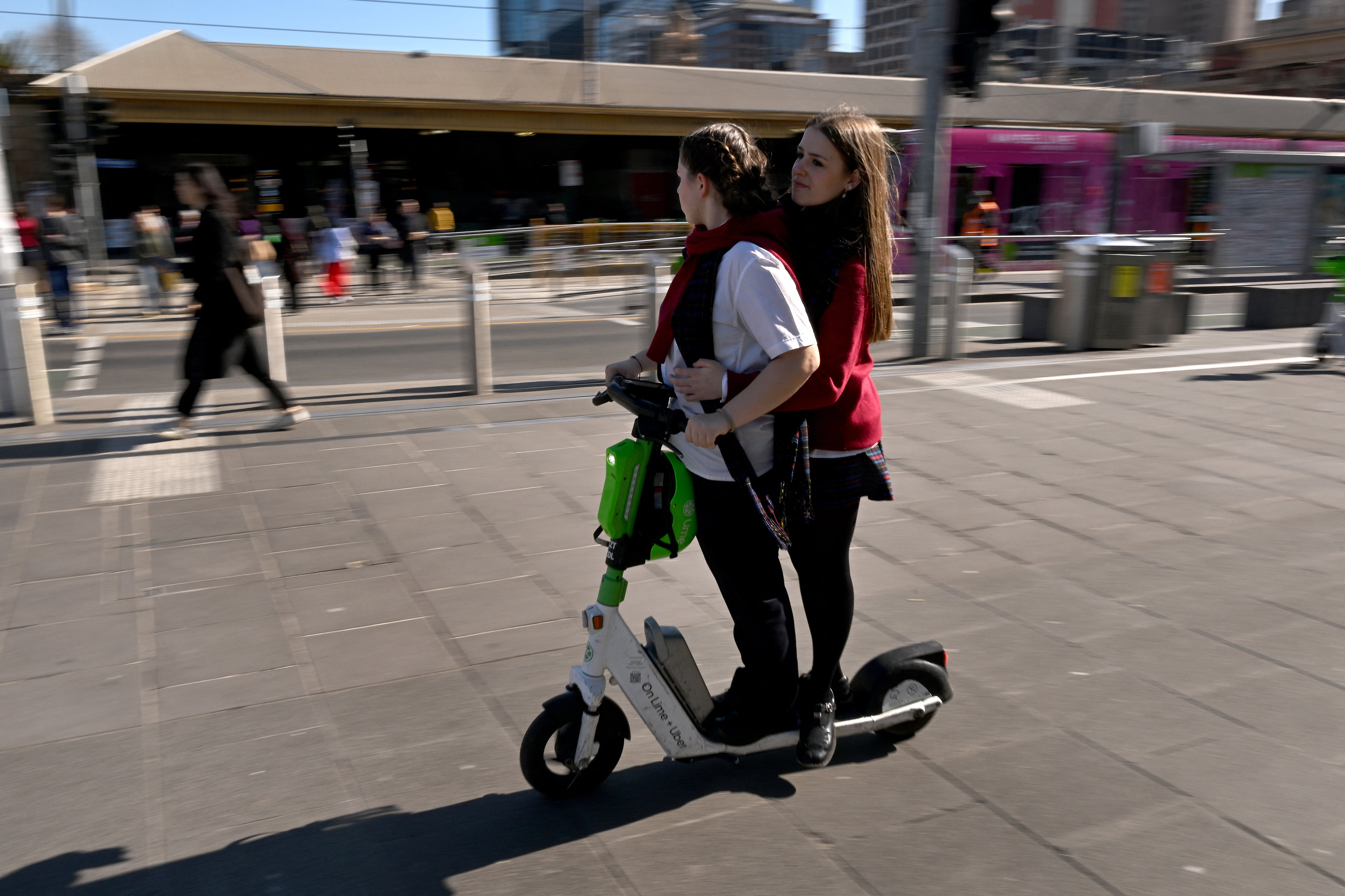 People ride a rental e-scooter in Melbourne on 13 August 2024