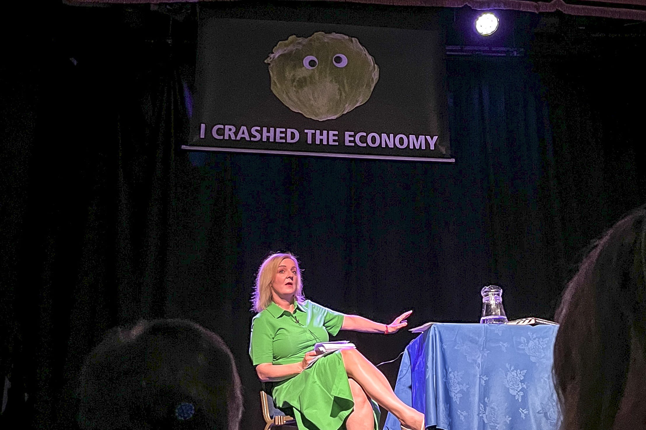 Former prime minister Liz Truss, as a banner featuring a picture of a lettuce unfurled behind her on the stage at an event in Suffolk (Led By Donkeys/PA)