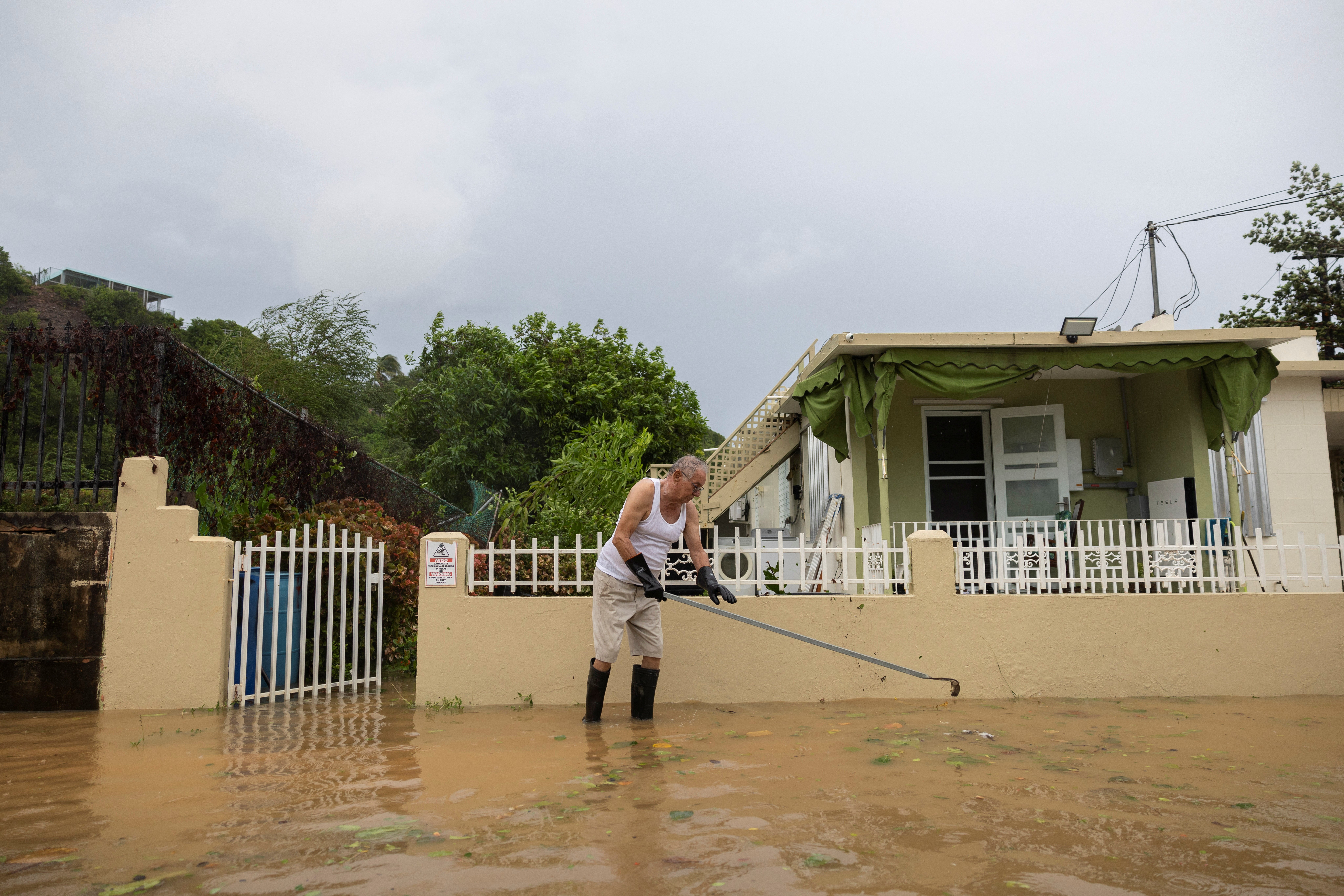 A man stands in floodwaters while clearing a drain blockage in Pajardo, Puerto Rico, Wednesday. Nearly 300,000 residents remain without power.