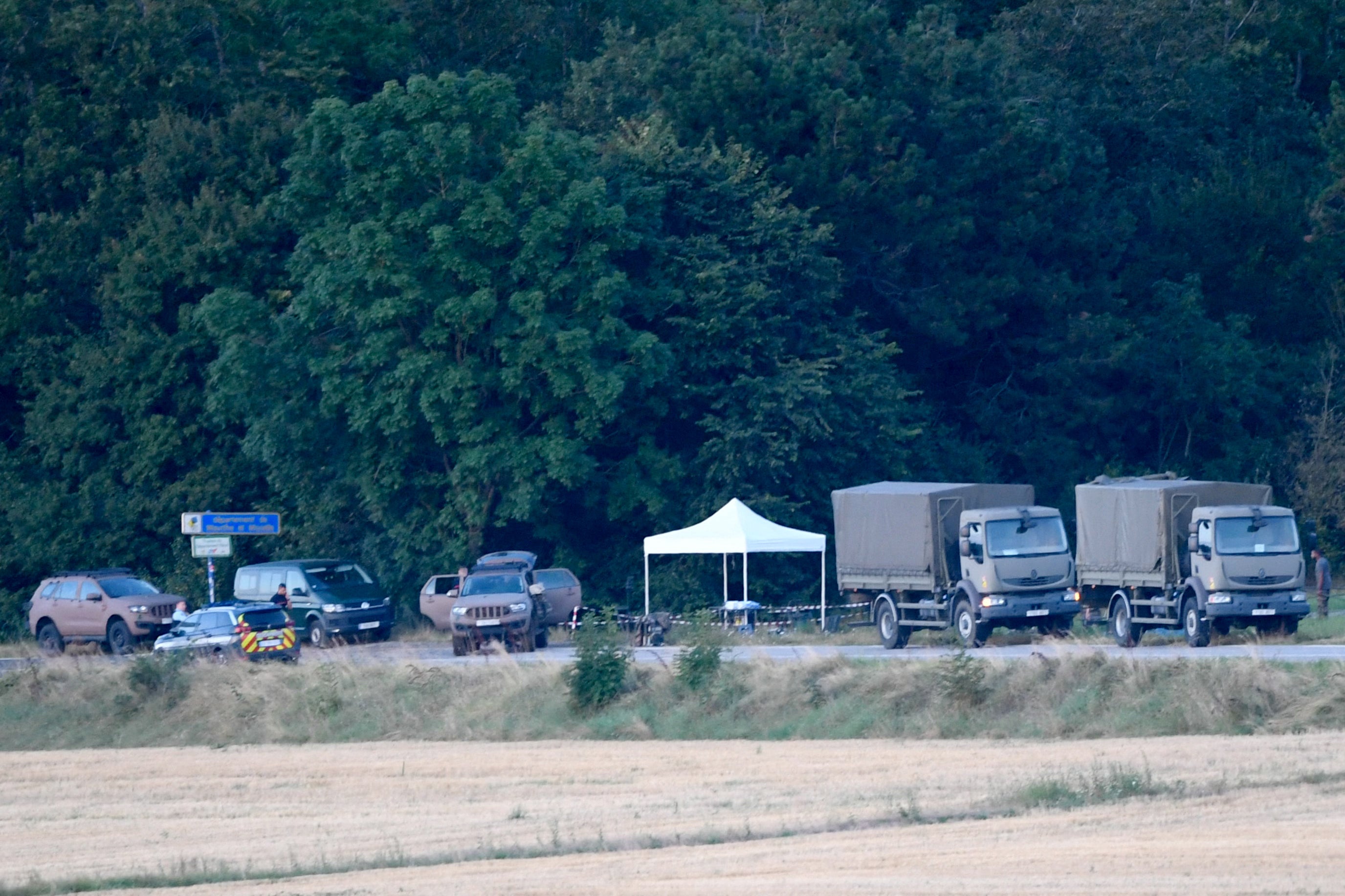 French gendarmes and French military vehicles stand beside the forest in Autreville, eastern France, on 14 August 2024, following a crash between two French military Rafale jets