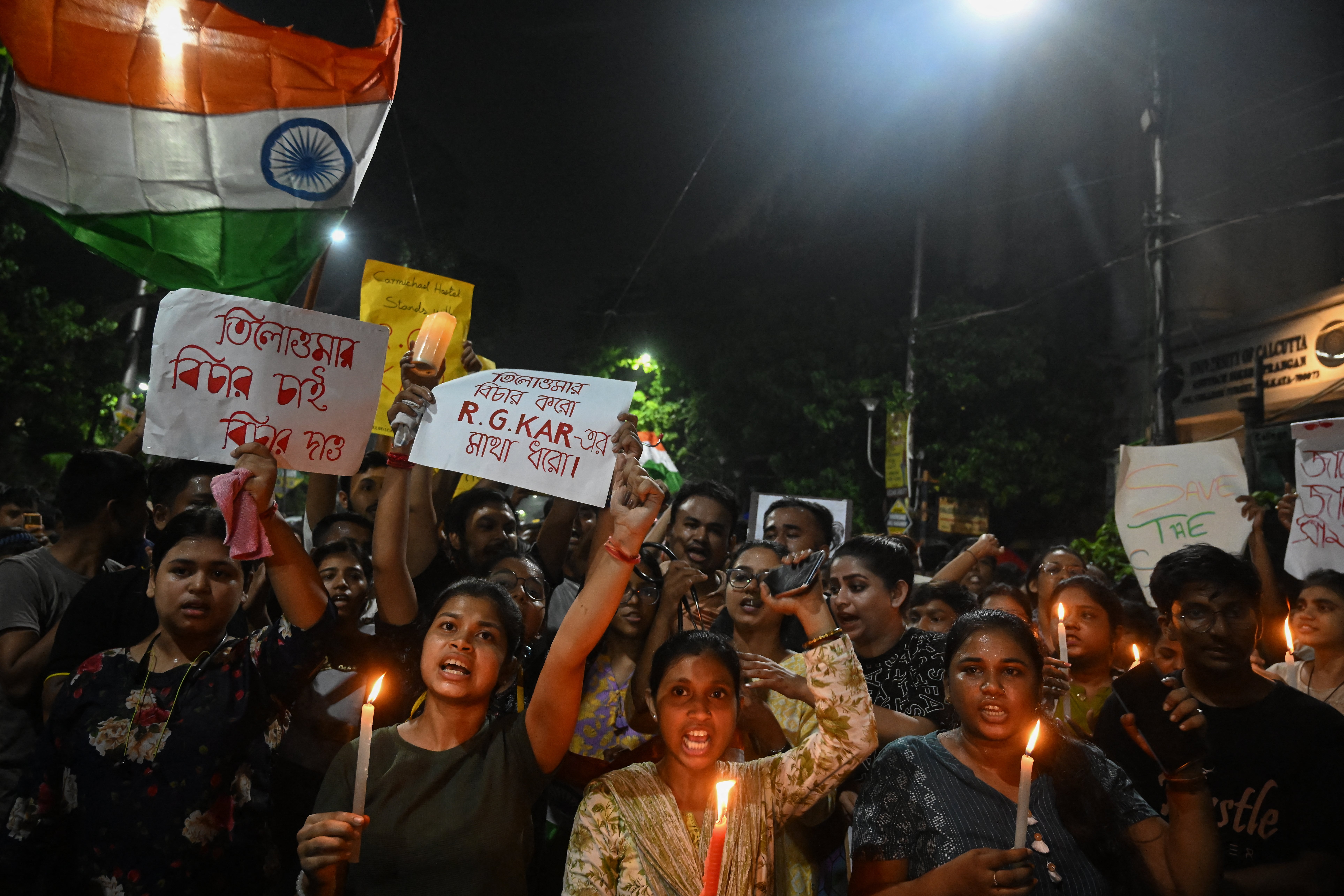 Medical professionals and activists hold posters and wave the Indian flag as they take part in a midnight protest