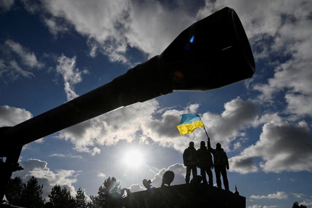 <p>Ukrainian personnel hold a Ukrainian flag as they stand on a Challenger 2 tank during training at Bovington Camp in southwestern Britain</p>