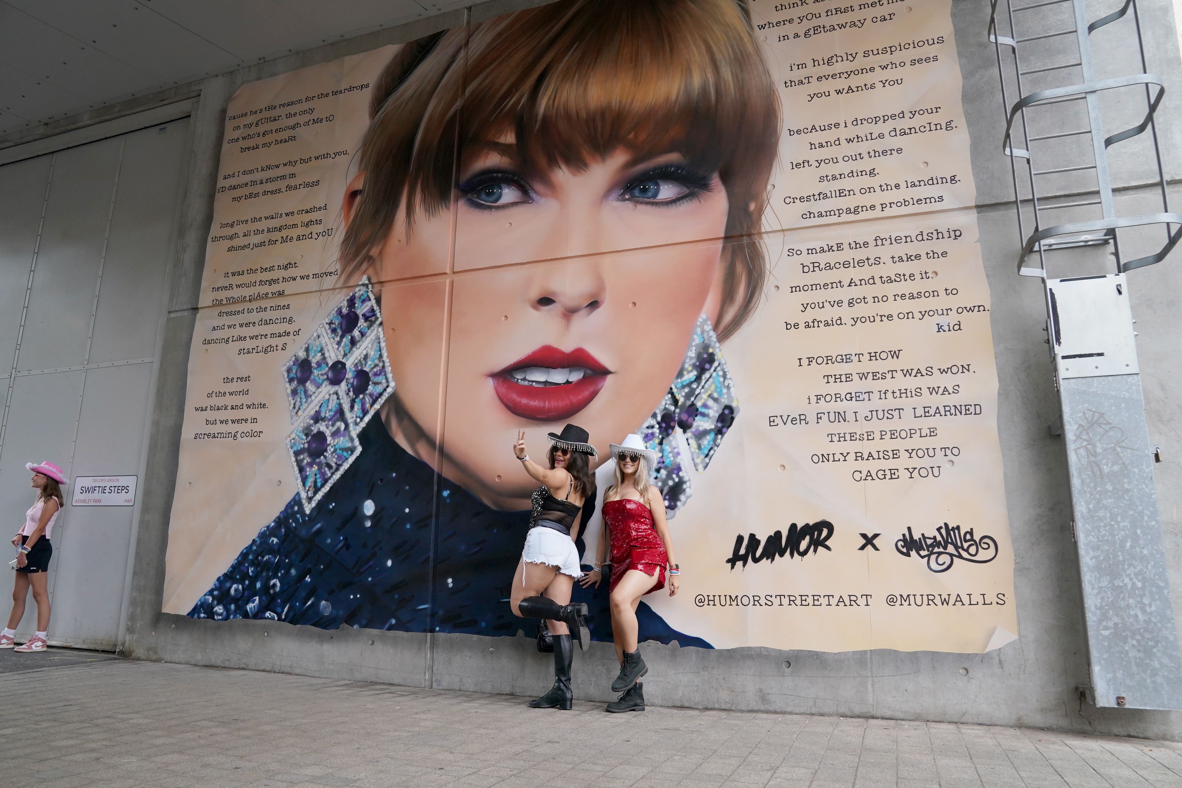 Fans pose in front of a mural of Taylor Swift at Wembley Stadium in London, ahead of Taylor Swift’s latest Eras Tour concert (Lucy North/PA)