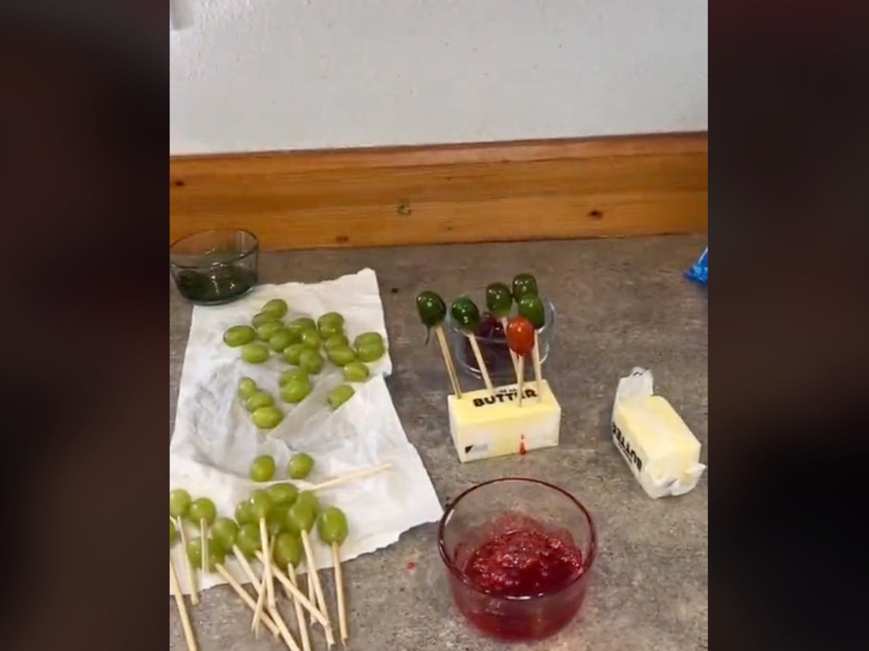 Several finished “candy grapes” cool while skewered into a stick of butter. The skewered grapes are dipped in the molten candy to create the candy, but the high temperature of the melted sweets has caused burns for TikTok users attempting the viral trend