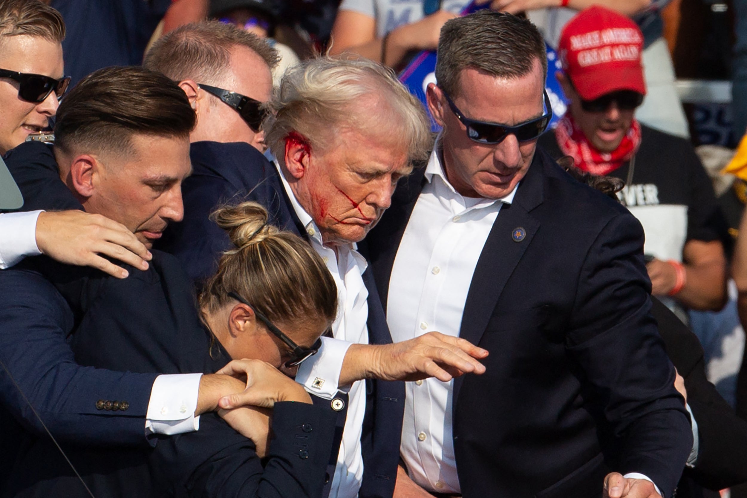 Donald Trump is seen with blood on his face as he is surrounding by secret service agents as he is taken off-stage at a campaign event in Butler, Pennsylvania, on July 13