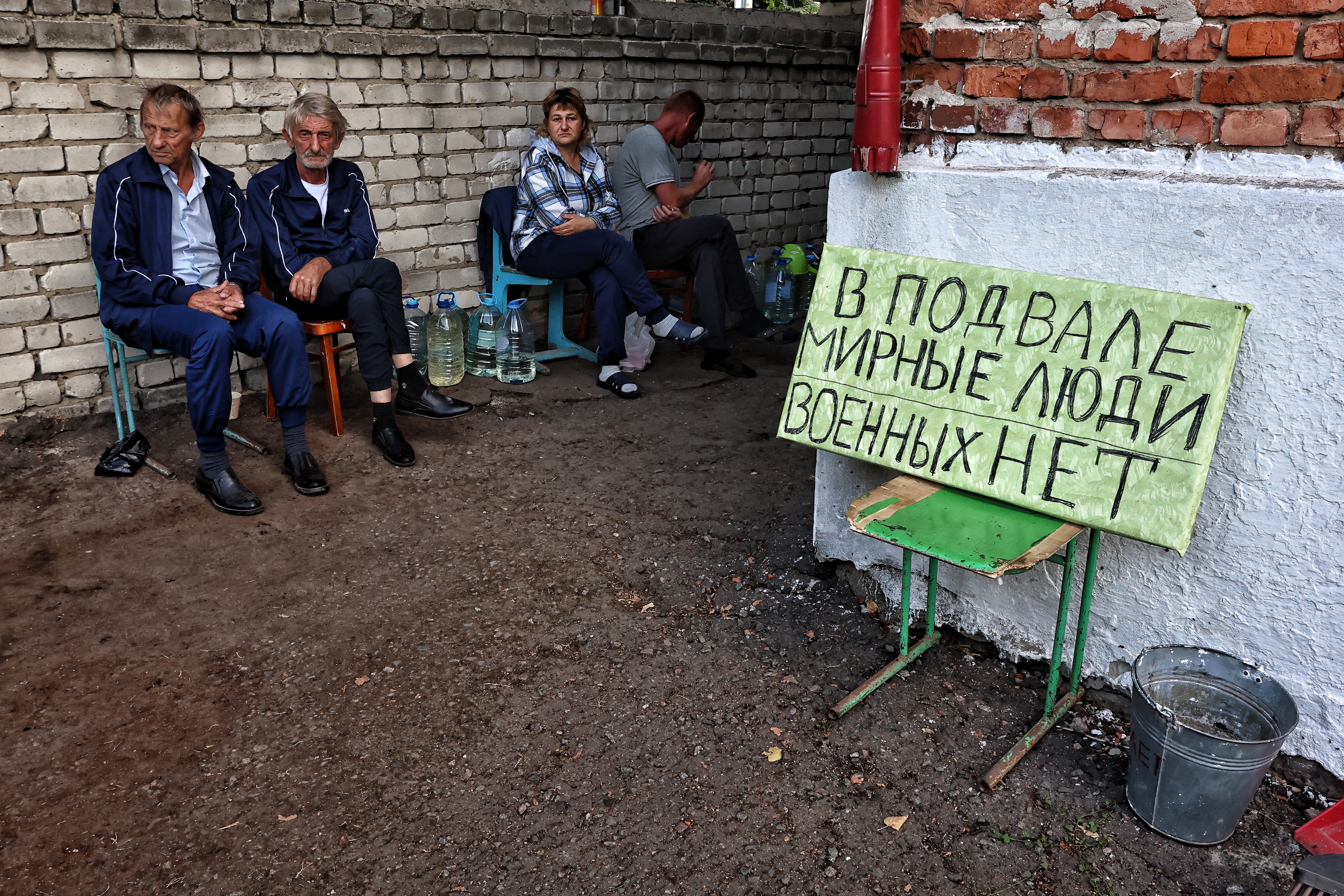 Photograph taken on 16 August, 2024, during a media tour organised by Ukraine, shows residents sitting next to a sign reading “There are civilians in the basement, no military” in the Ukrainian-controlled Russian town of Sudzha, Kursk