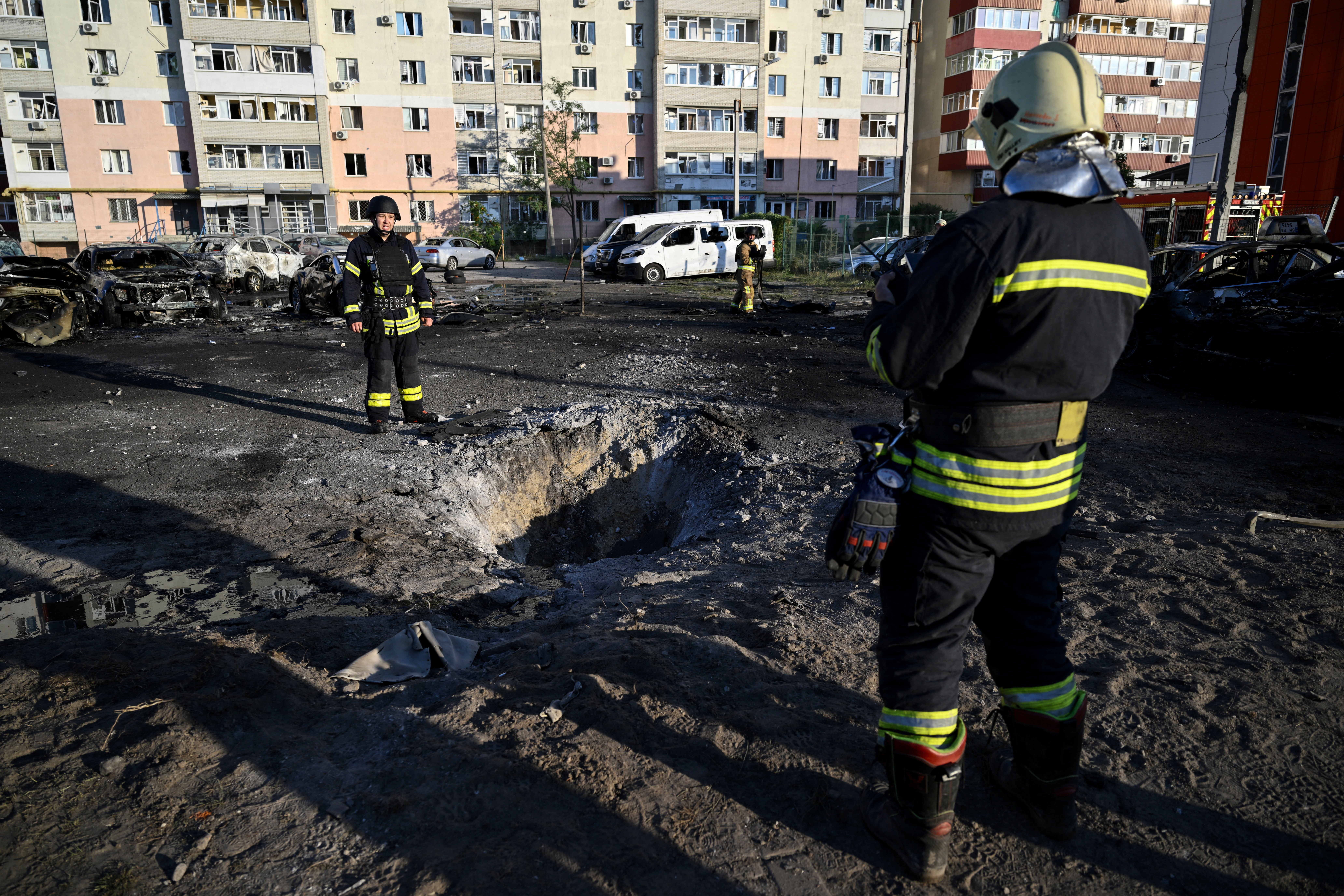 Firefighters stand next to a hole following a Russian strike in the city of Sumy on August 17, 2024, amid the Russian invasion of Ukraine