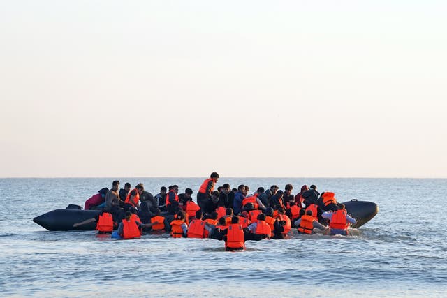 <p>A group of people thought to be migrants wade through the sea to clamber aboard a small boat off the beach in Gravelines, northern France</p>