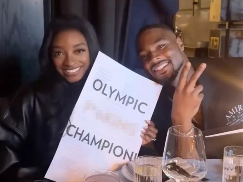 Simone Biles poses with her husband in a restaurant with the menu reading 