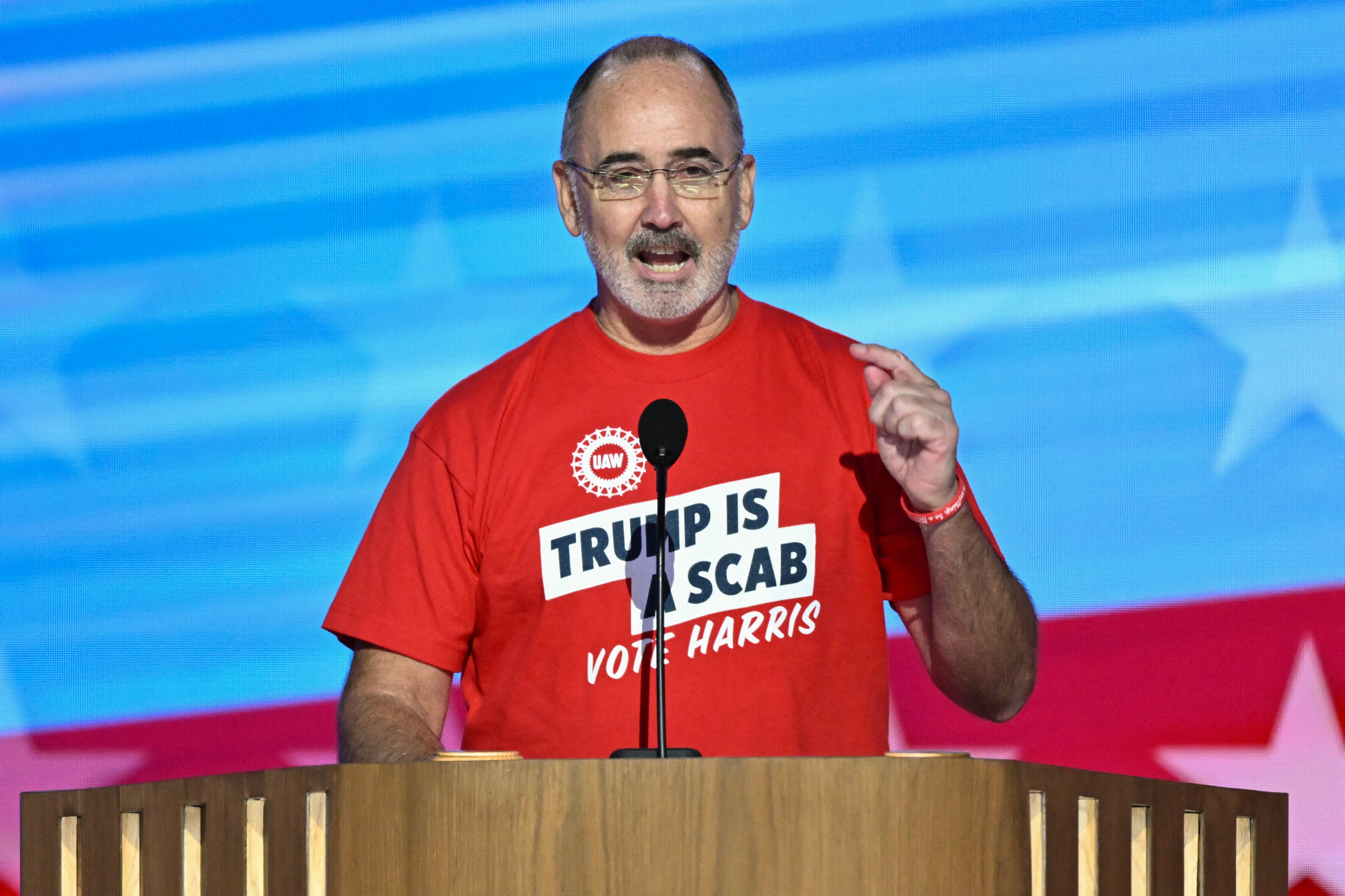 United Auto Workers union president Shawn Fain speaks to the Democratic National Convention on August 19. He removed his jacket revealing a T-shirt that read ‘Trump is a scab’