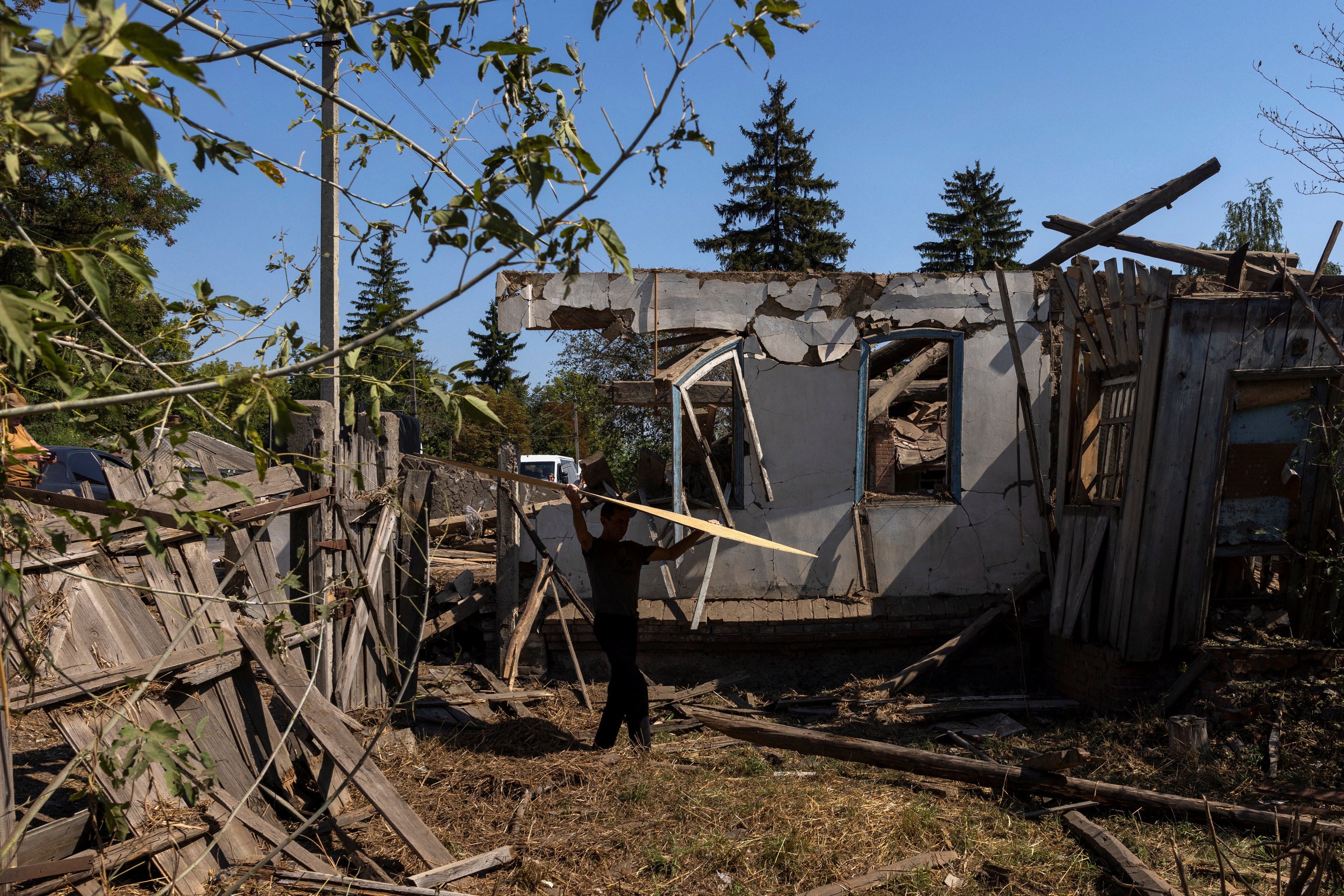 A man carries a board for a damaged house past a residential building that was destroyed in a recent Russian airstrike in Bilopillia near the Russian border