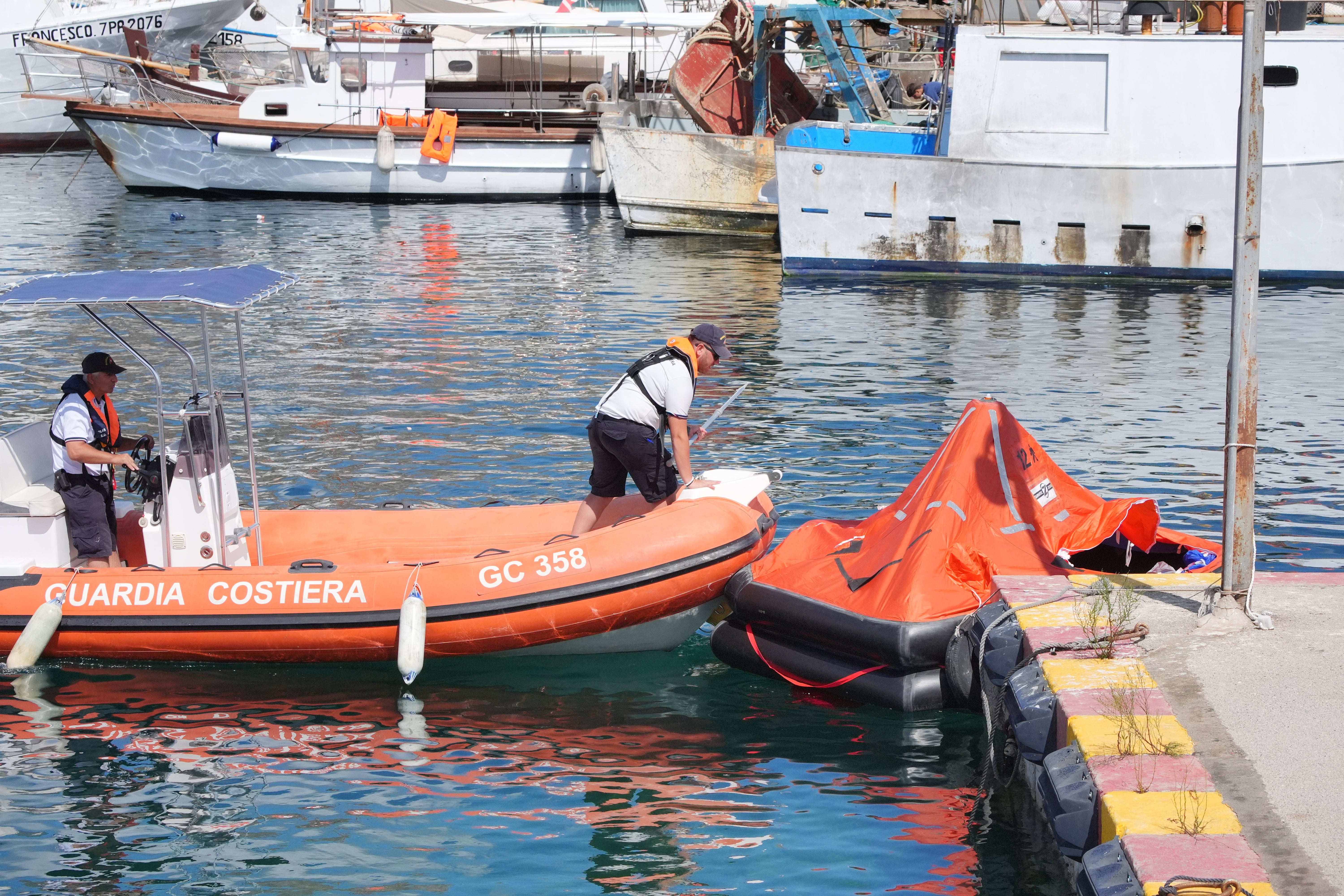 The Coast Guard wrangle a rapid inflatable emergency lifeboat in Porticello Harbour on the Sicilian coast where the search continues for British technology tycoon Mike Lynch and his daughter Hannah, who are among six tourists missing after a luxury yacht sank in a tornado off the coast of Sicily