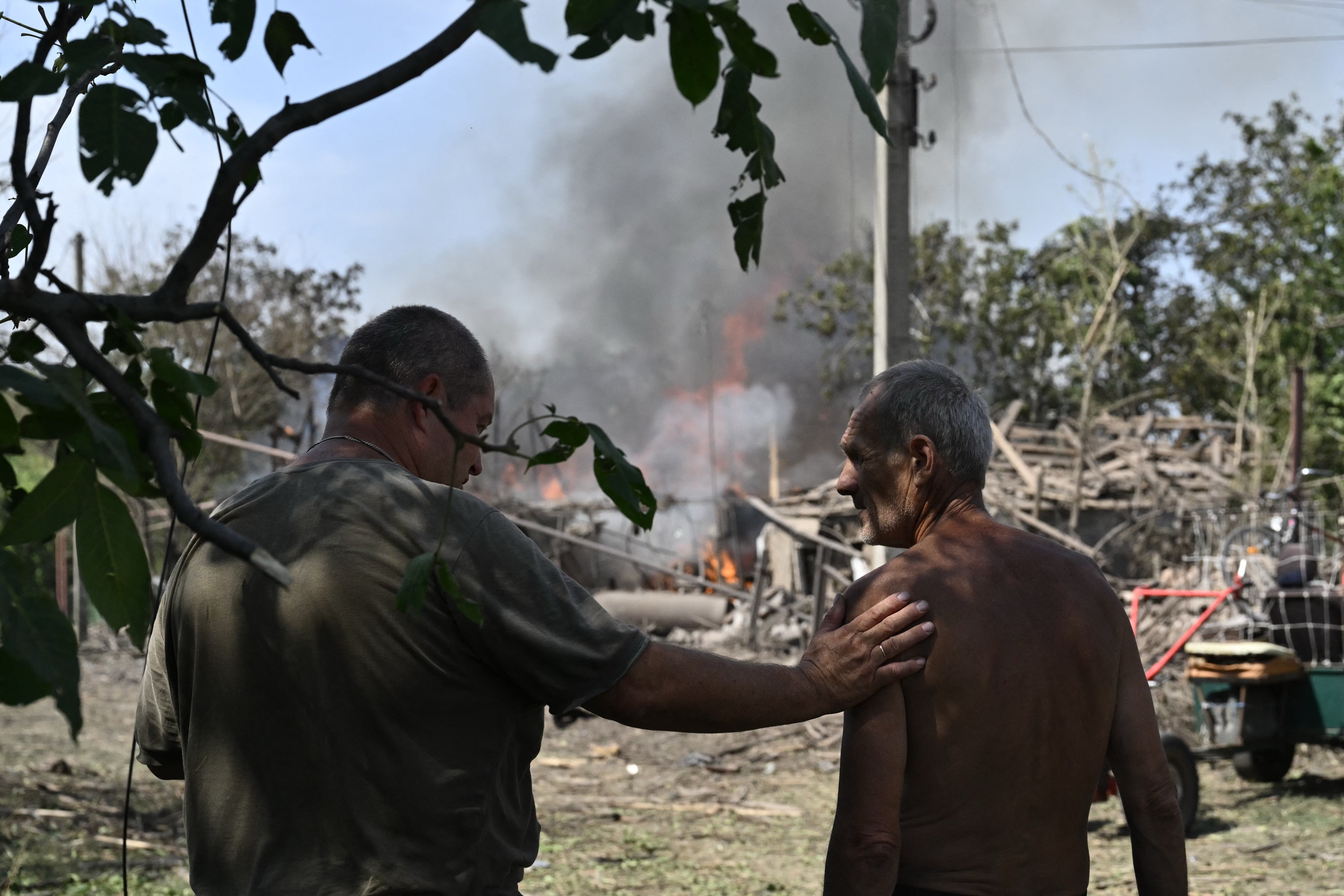 Local residents stand next to a burning private house a day after a missile attack in Myrnograd, Donetsk region,