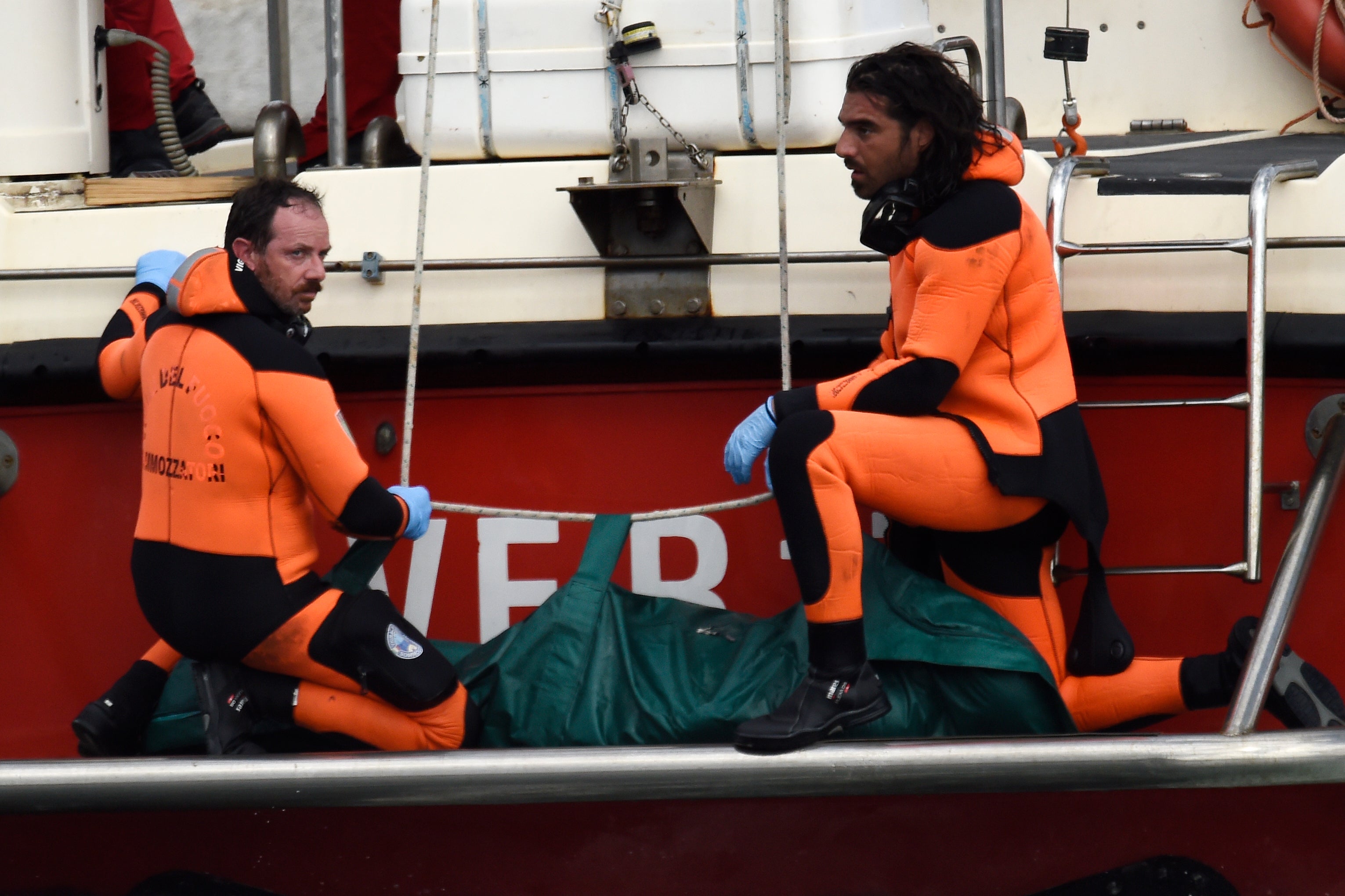 Italian firefighters divers carry the body of one of the victims from the British ship to shore, in a green bag. 