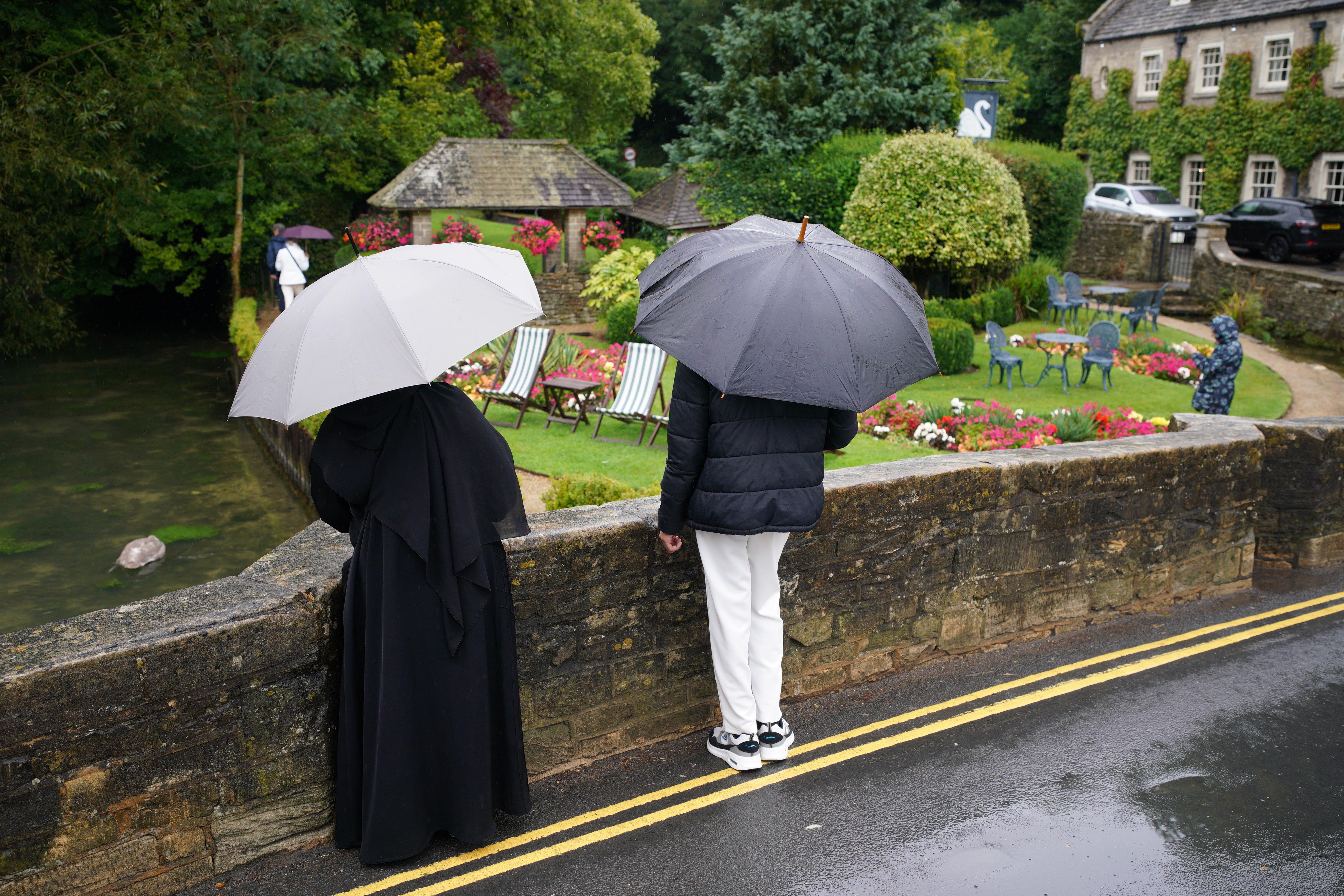 Visitors with umbrellas in the rainy weather at Bibury village in Gloucestershire (Ben Birchall/PA)