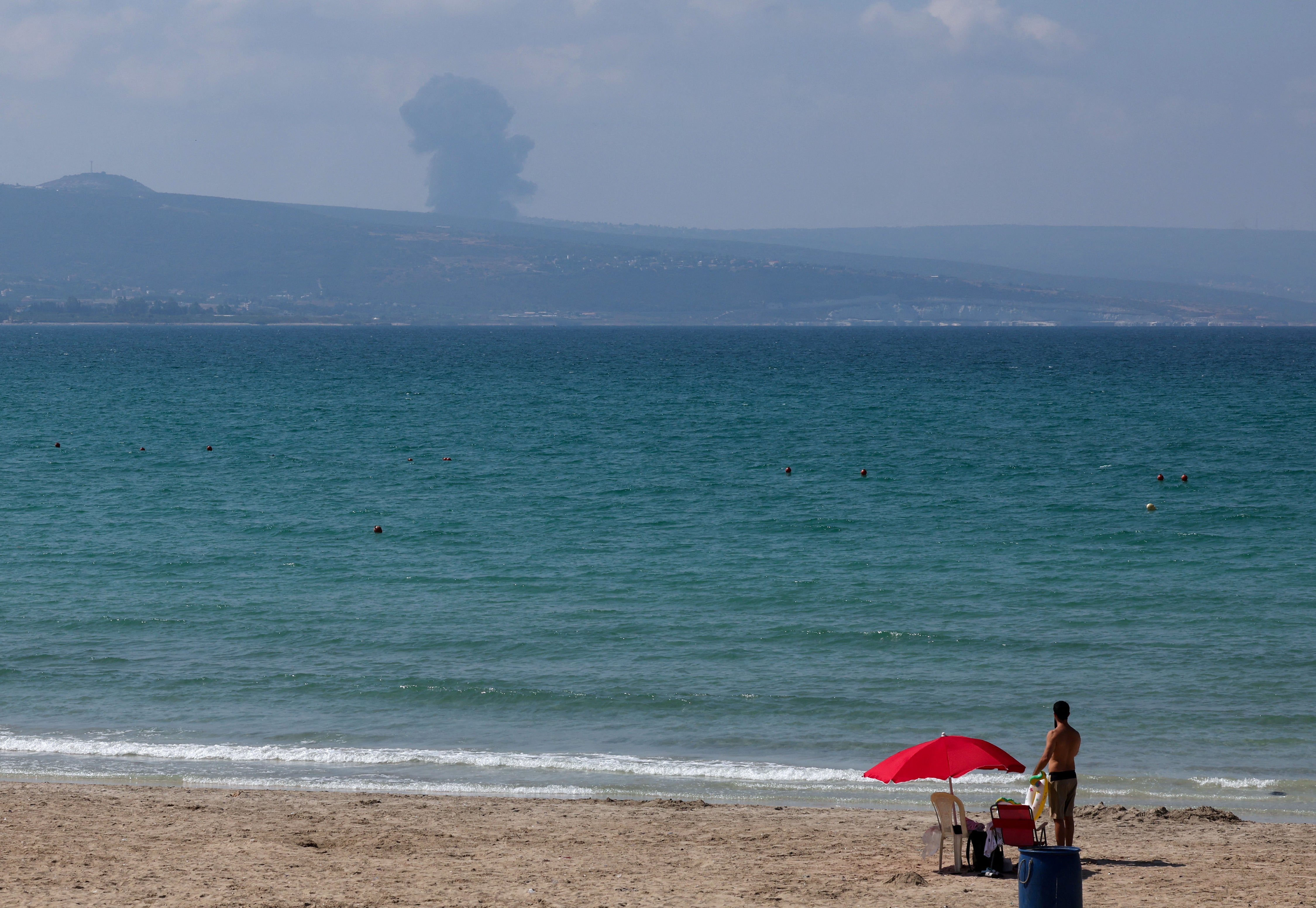 A view shows smoke on the Lebanese side of the border with Israel, as a man stands at a beach in Tyre, amid ongoing cross-border hostilities between Hezbollah and Israeli forces, southern Lebanon