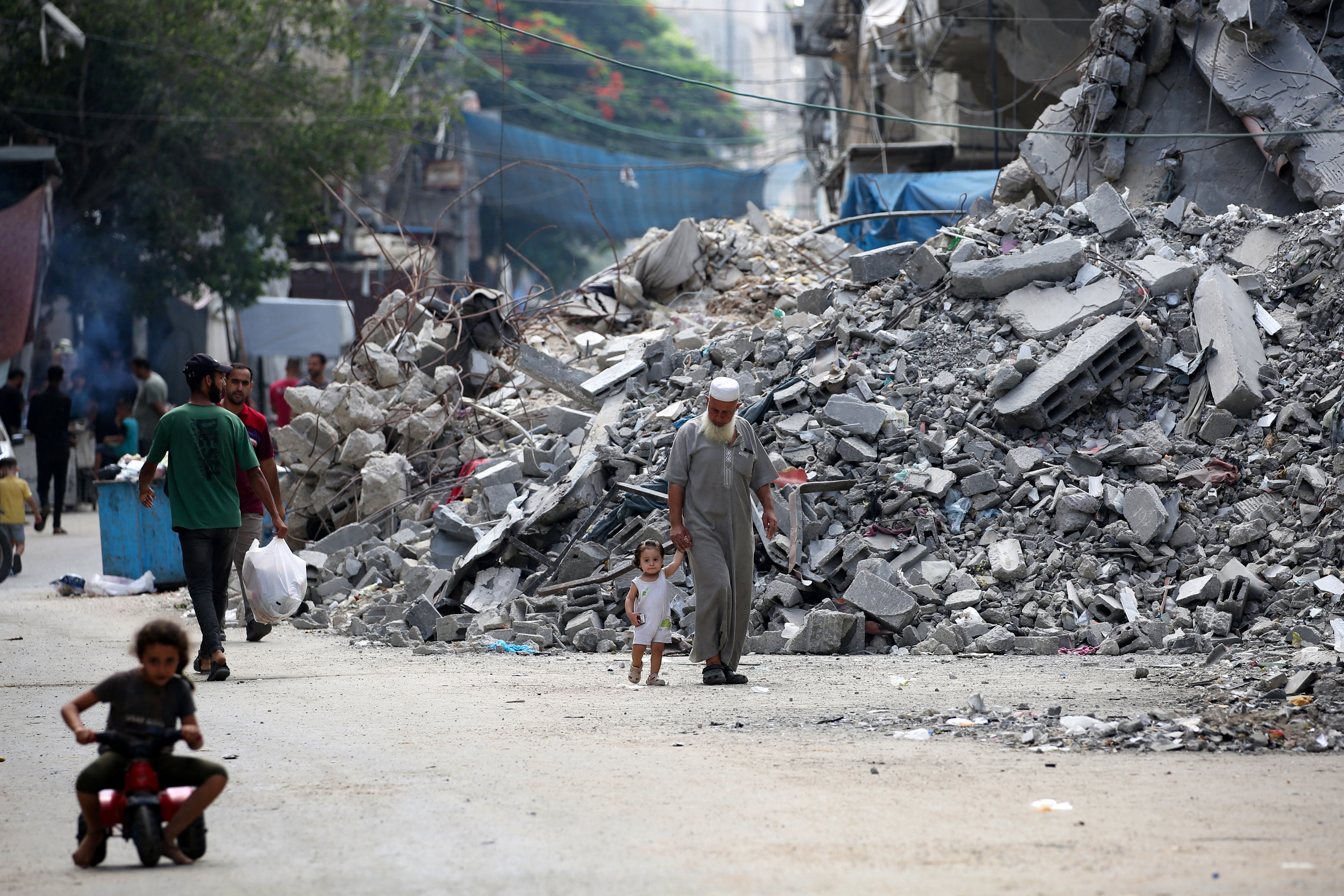 An elderly man holds a child by the hand as he walks past a building levelled by Israeli bombardment in the Bureij refugee camp in central Gaza Strip