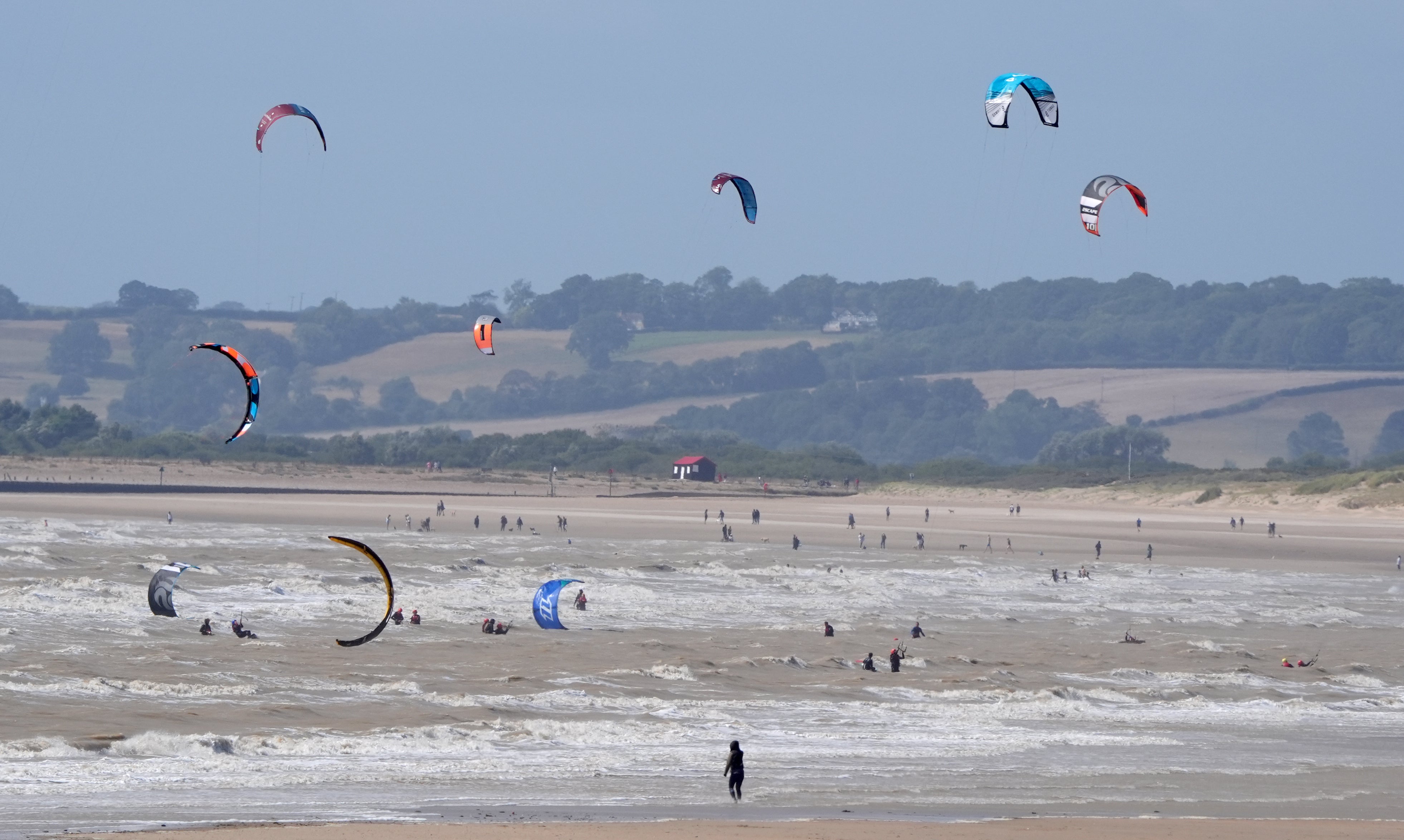 Kite surfers enjoy the windy conditions on the sea at Camber Sands in East Sussex