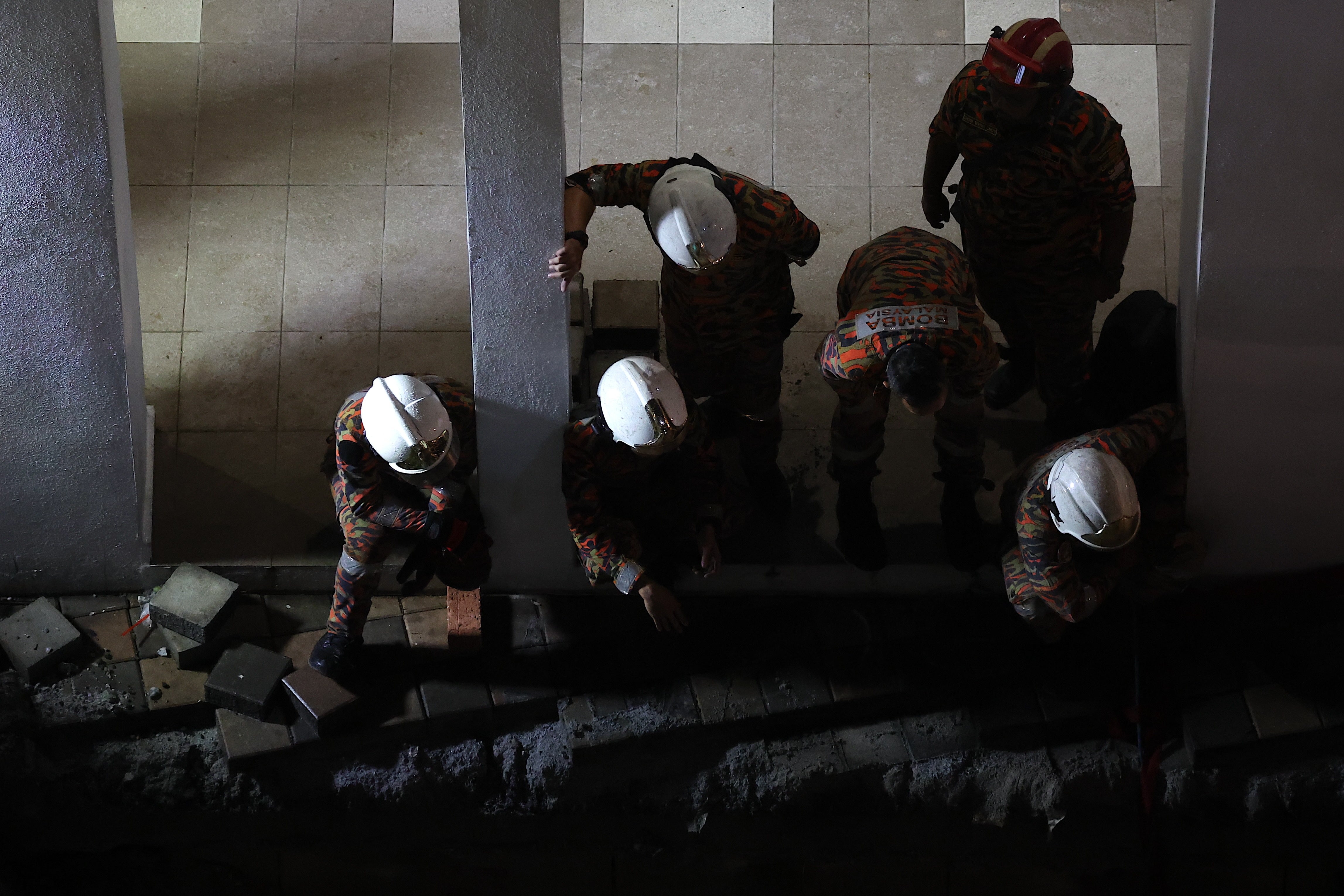 Malaysia Fire and Rescue Department officers inspect the site where a woman fell into a sinkhole and vanished