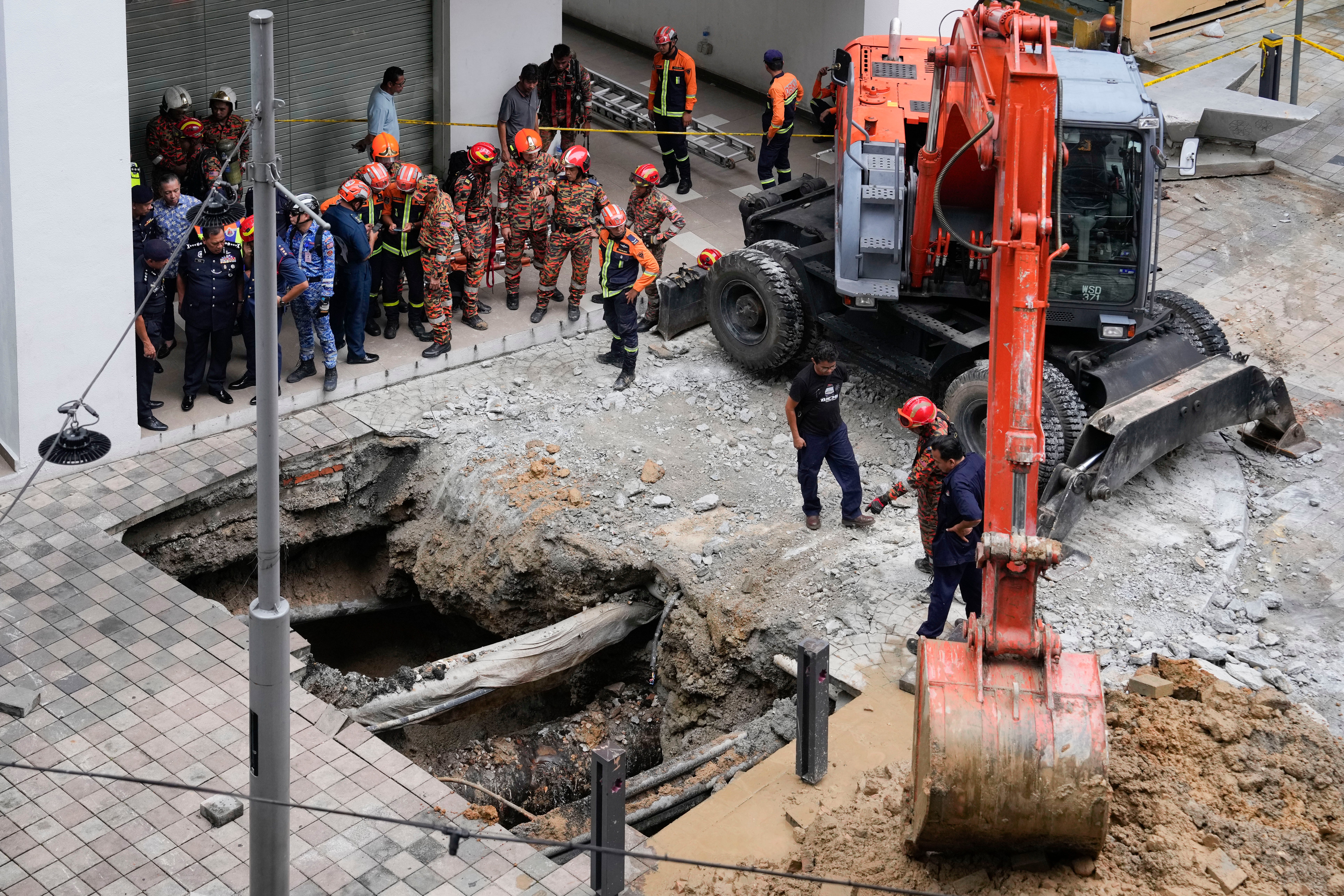 Fire and rescue department workers use crane to dig after receiving reports that a woman has fallen into a sinkhole after a section of the sidewalk caved in in Kuala Lumpur on Friday, 23 August 2024