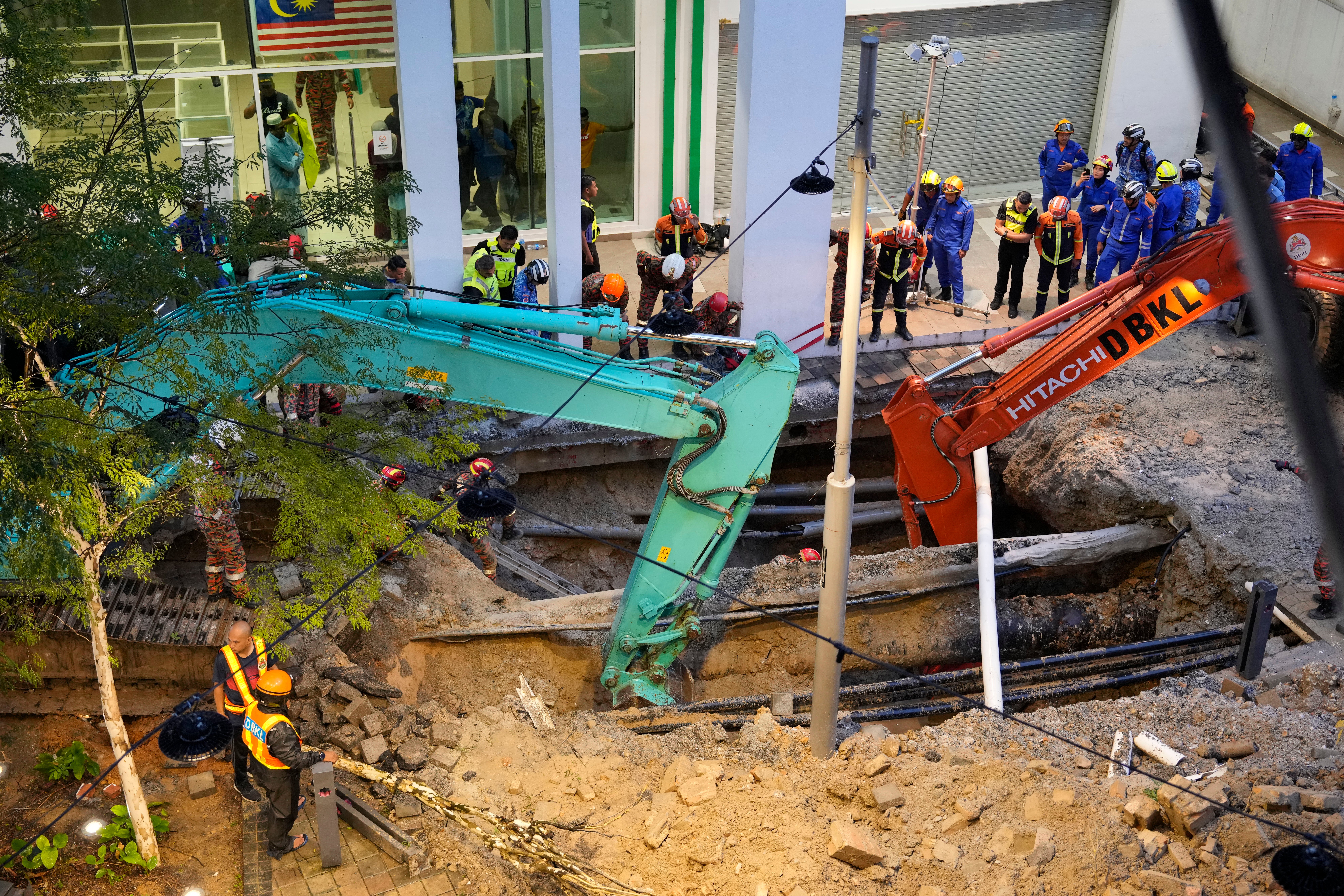 Fire and Rescue department use crane to dig a deep sinkhole after receiving reports that a woman has fallen into the sinkhole after a section of the sidewalk caved in Kuala Lumpur, Friday, 23 August 2024