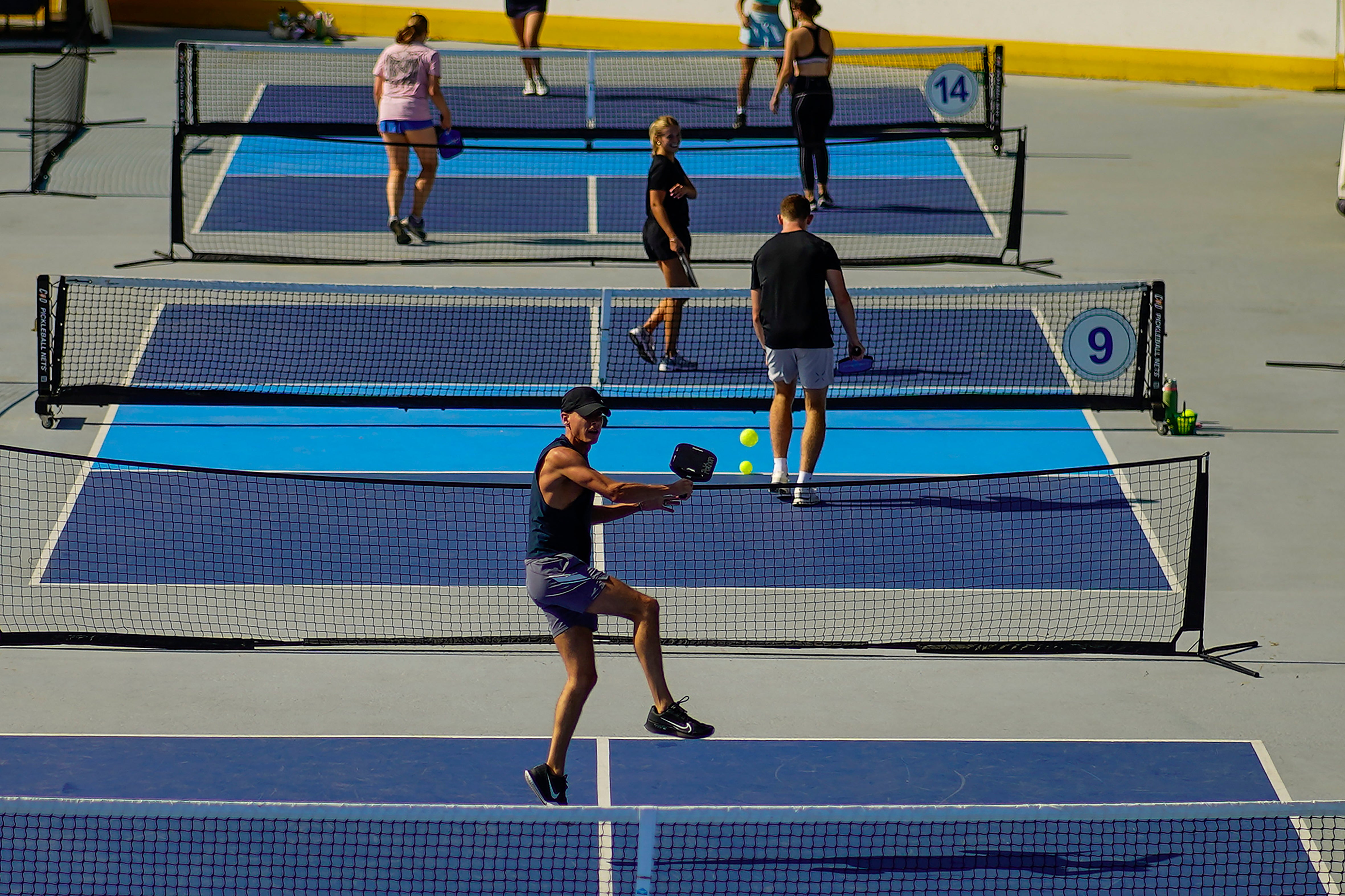 A man jumps to return the ball as people practice pickleball on the courts of CityPickle at Central Park's Wollman Rink, Saturday, Aug. 24, 2024