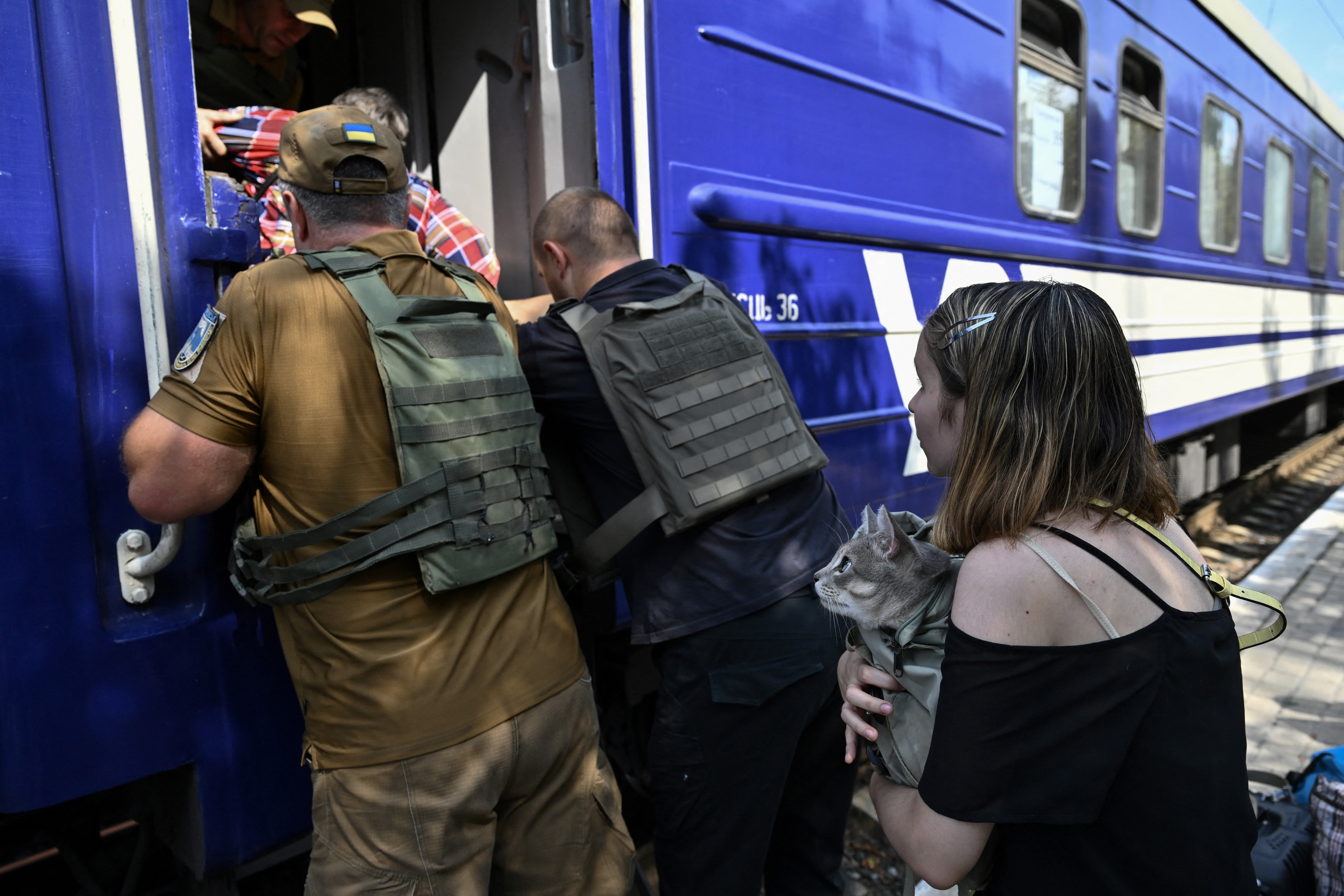 Officials assist a an elderly woman to board an evacuation train as a teenager carrying a cat waits at an undisclosed location in Donetsk region