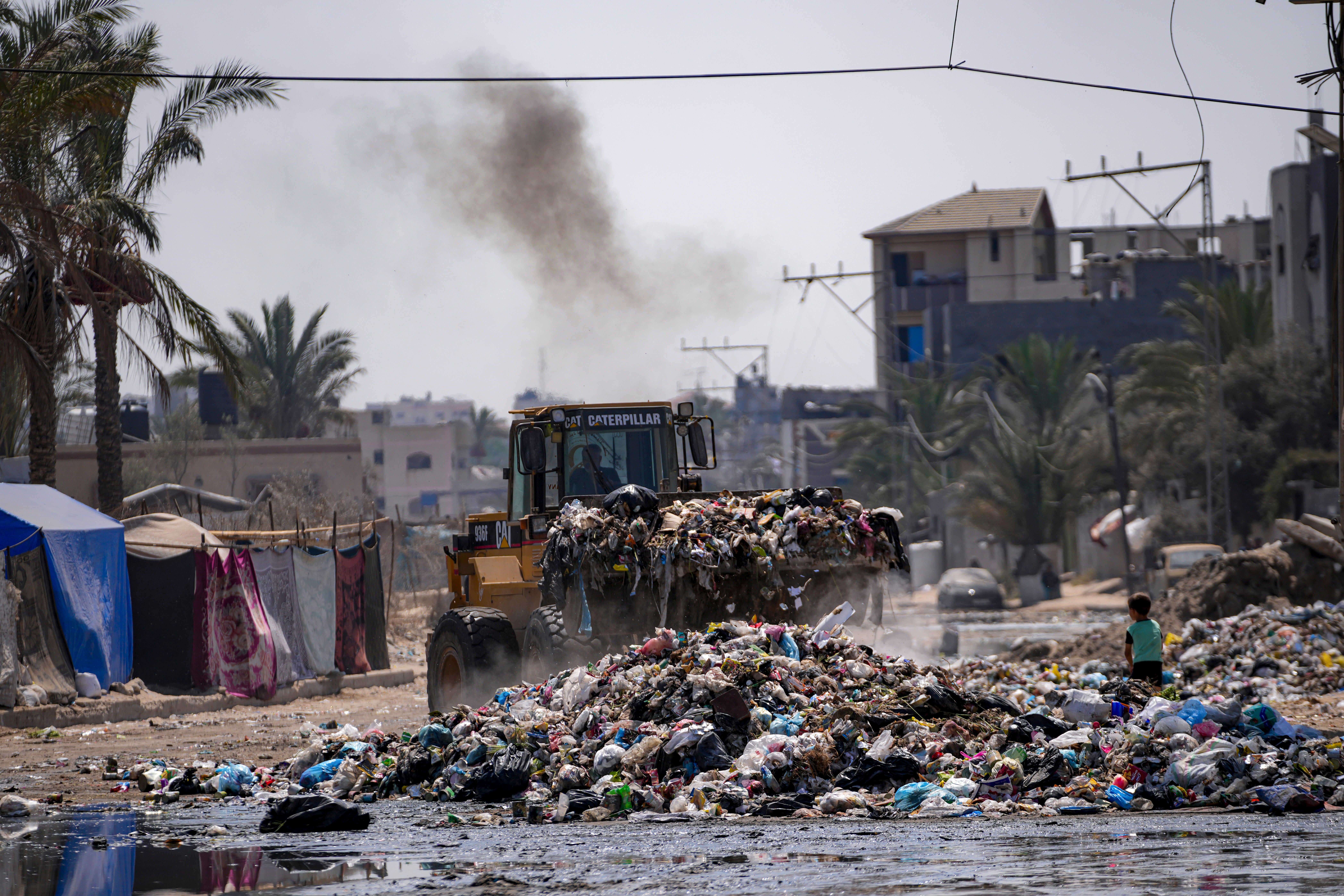 A bulldozer cleans up plastic and other waste materials at a street in Deir al-Balah, central Gaza Strip, 27 Aug 2024