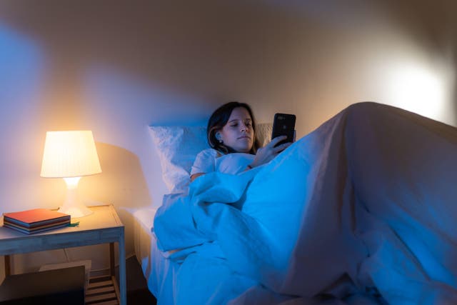 <p>Girl looking her smart phone doom scrolling on bed in the middle of the night (Alamy/PA)</p>