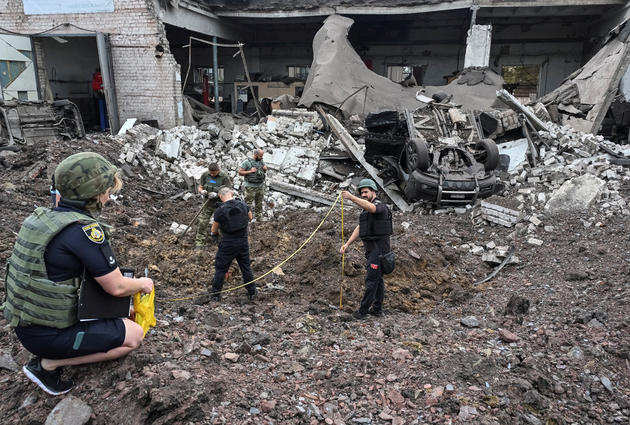 Two experts hold a tape measure over the blast radius of crater following a Russian attack on Kryvyi Rih