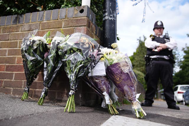 A police officer stands by a police cordon and floral tributes on Overbury Street, near the scene in Rushmore Road, Clapton, east London, after a man was stabbed to death (Aaron Chown/PA)