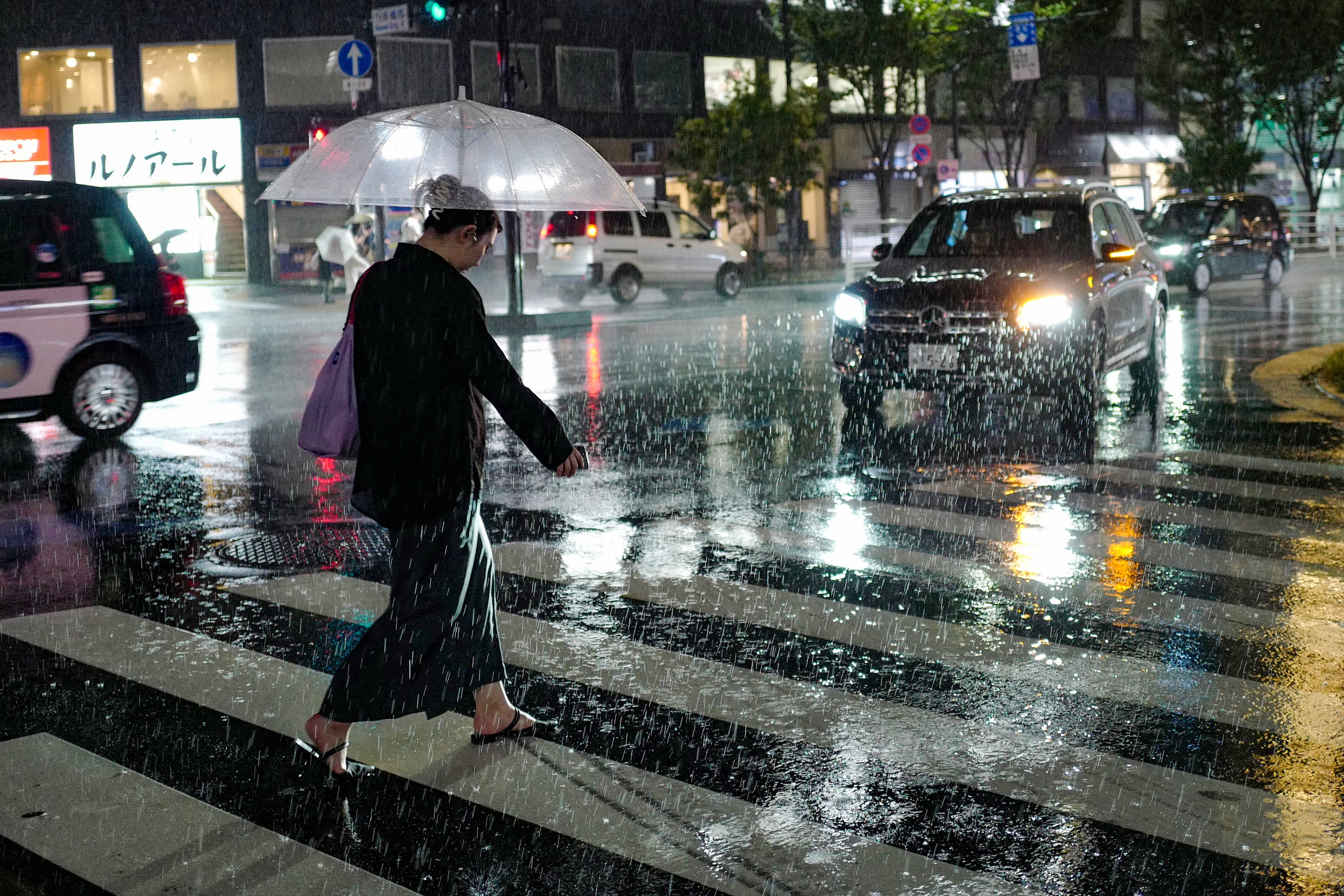 A woman walks across a street amid heavy rainfall in Tokyo